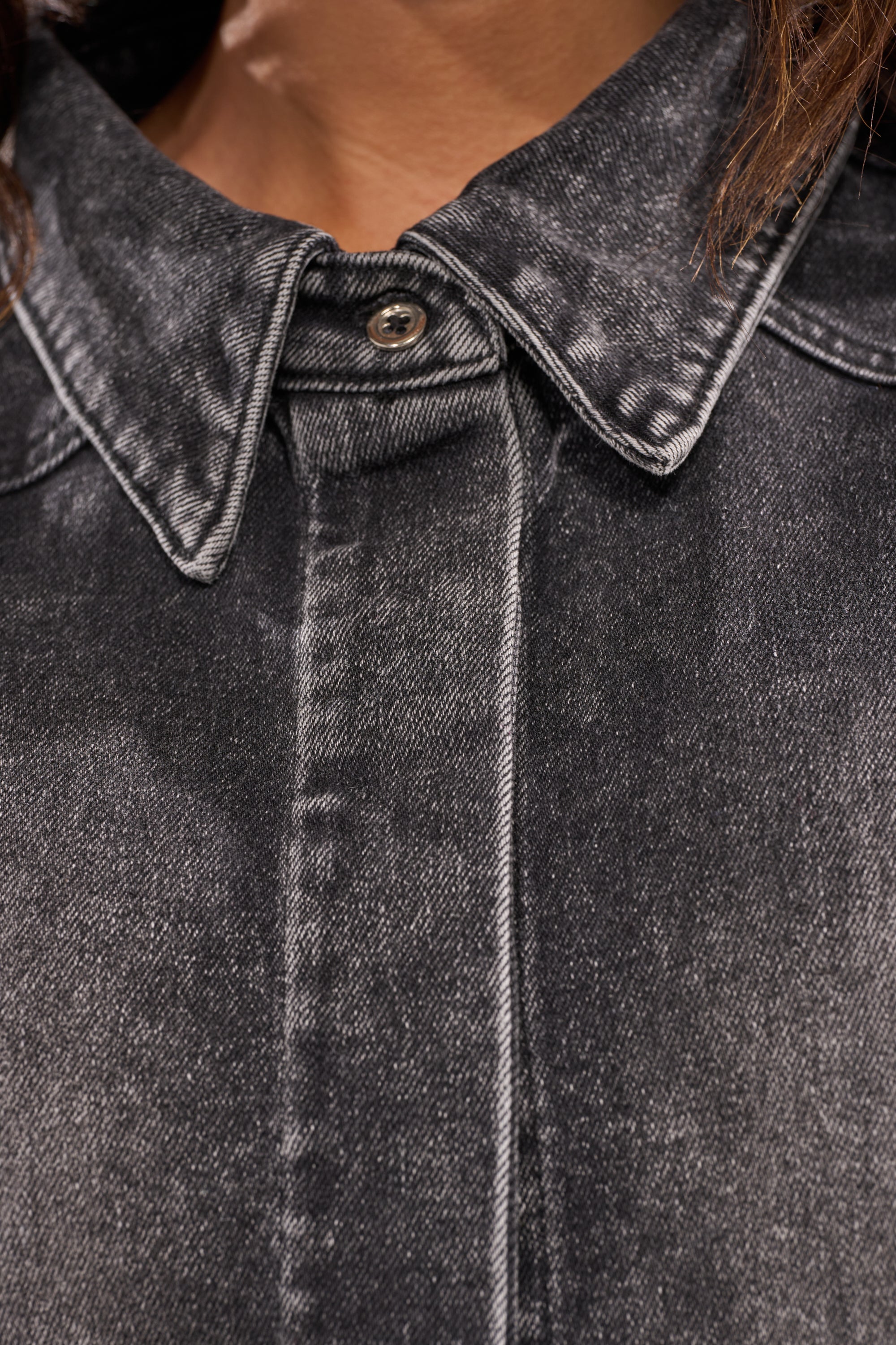 Close-up of a person wearing the IN MY OWN WORLD BUTTON DOWN, a retro denim shirt featuring a pointed collar, visible top button, and subtly faded textured fabric. Only the person's neck and lower face are shown. 11
