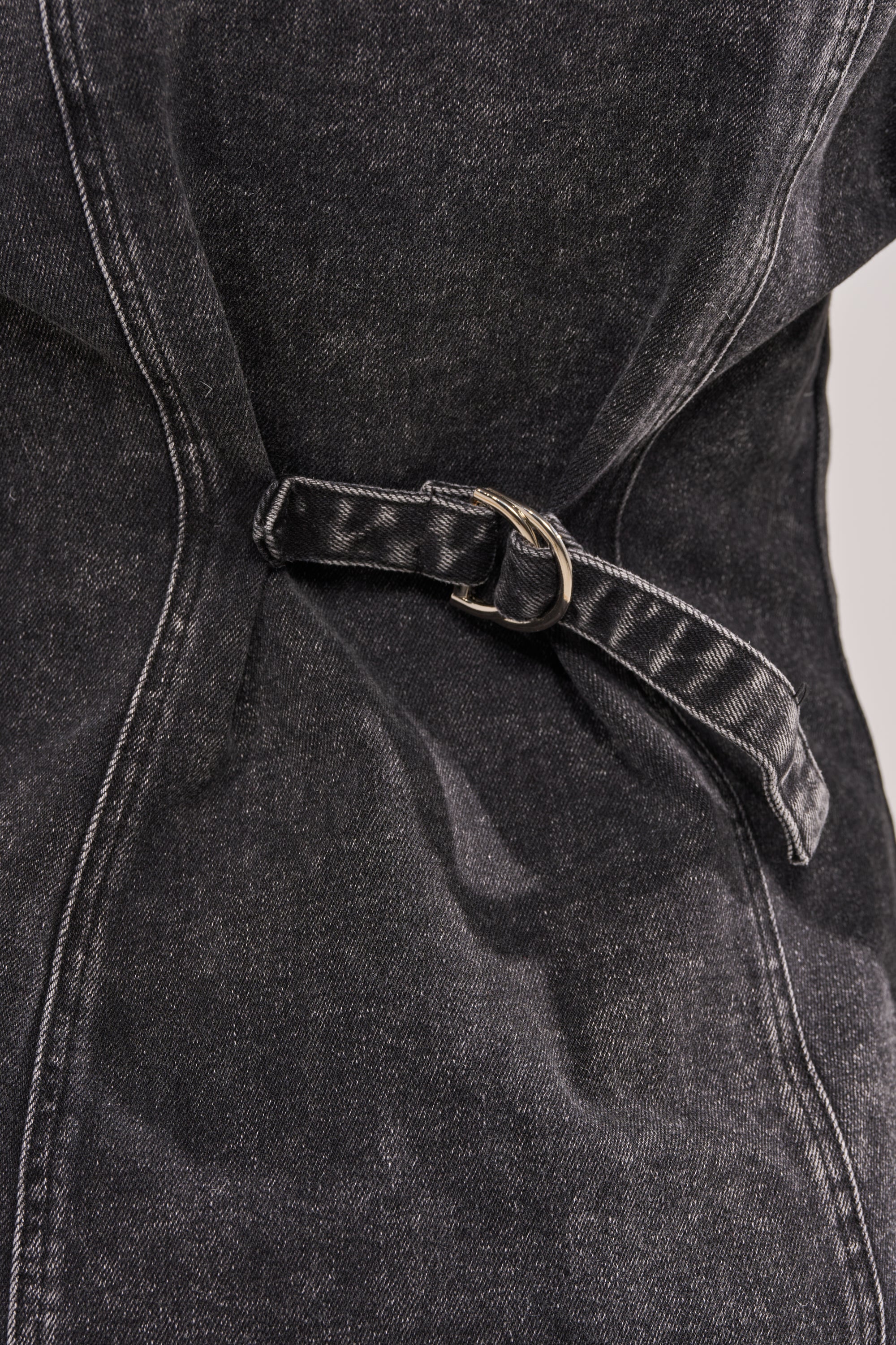 Close-up of the IN MY OWN WORLD BUTTON DOWN in dark denim, featuring an adjustable strap with a silver buckle on a fabric belt, and highlighting visible stitching and material folds. 12