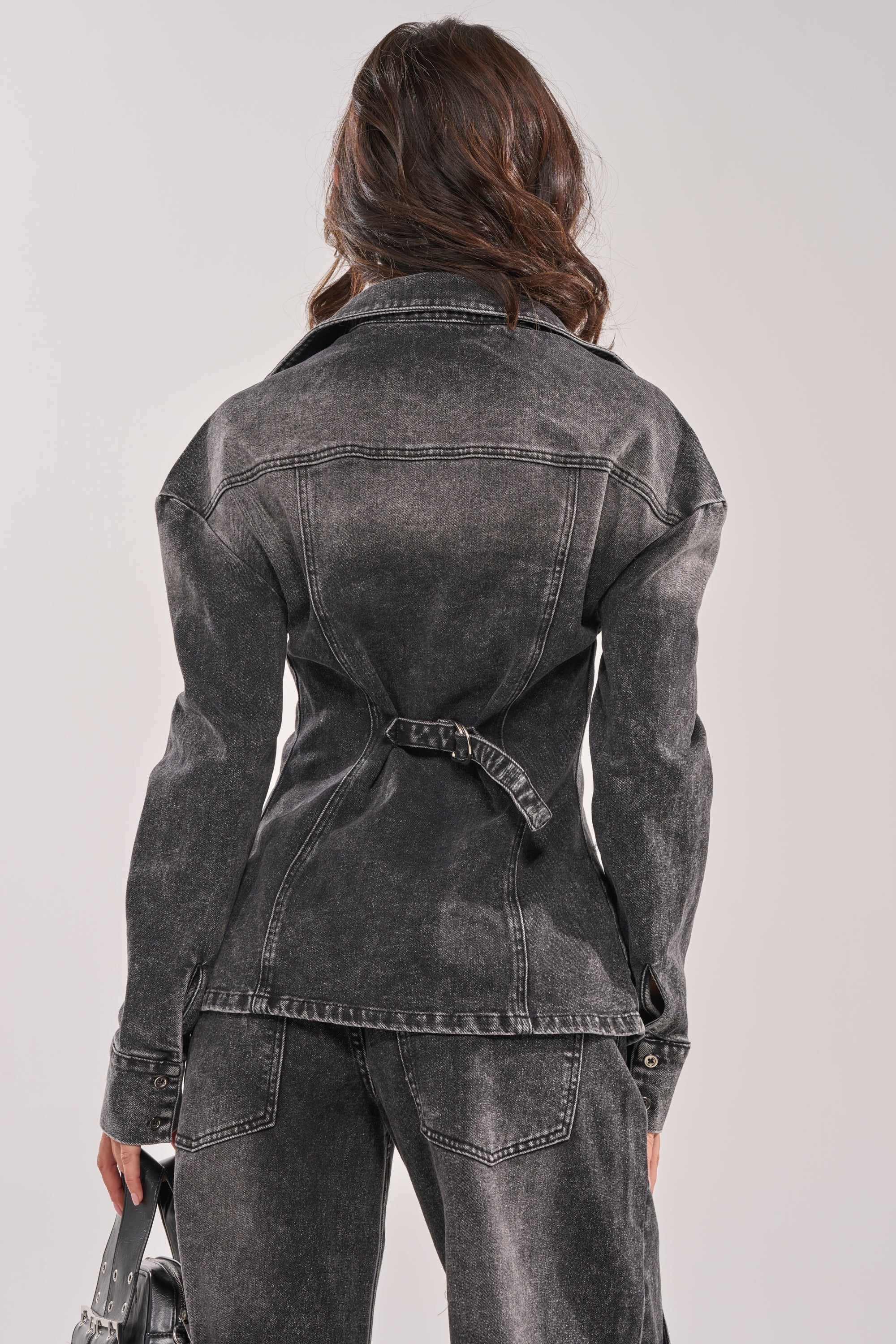 A person with wavy brown hair wears the IN MY OWN WORLD BUTTON DOWN in washed black denim and matching pants, standing with their back to the camera and holding a small bag in their left hand. 7