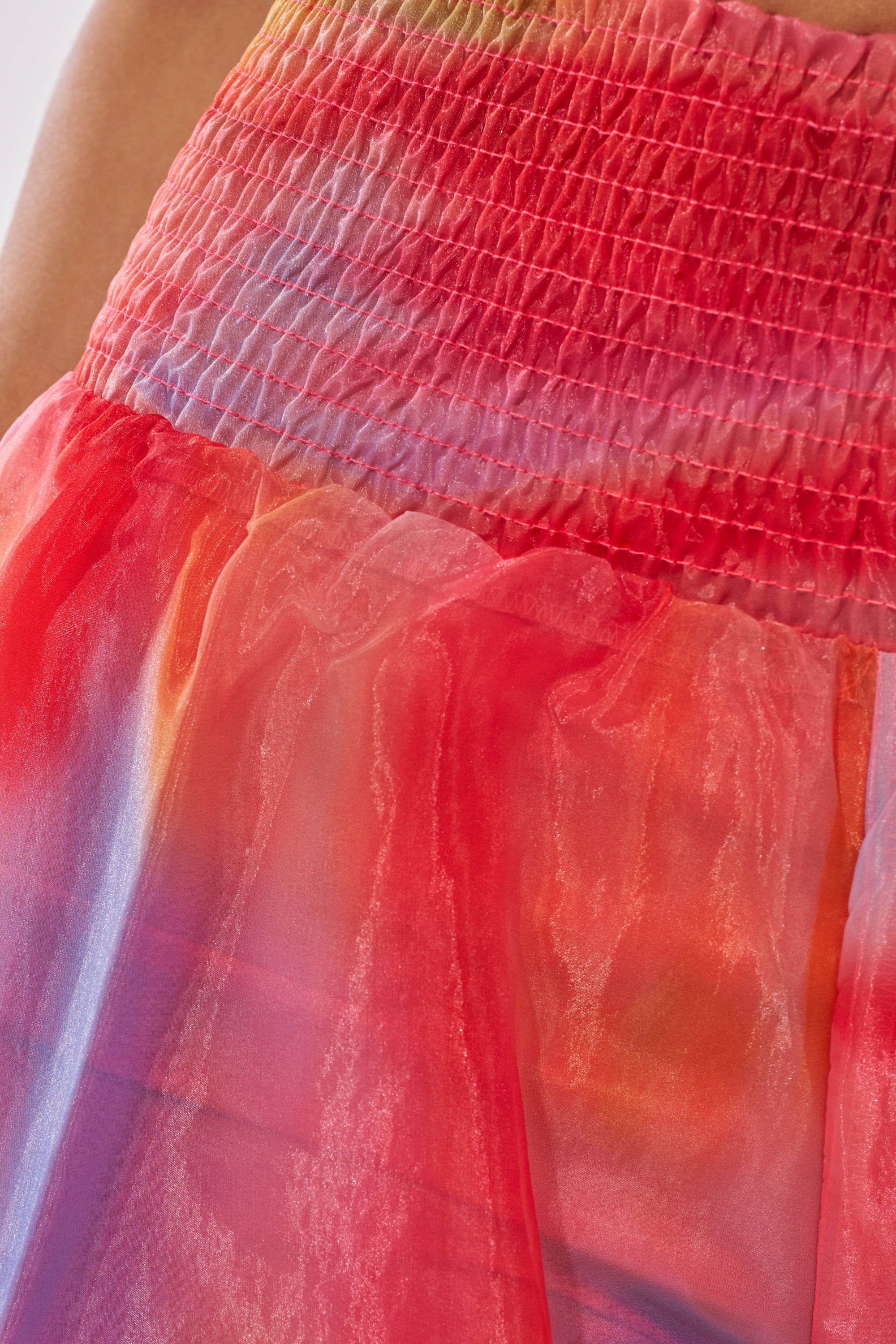 Close-up of the INTERESTED IN YOU PALAZZO PANT, featuring a smocked high-rise waistband and sheer organza that blends red, orange, blue, and purple hues for a vibrant, flowing look. 7