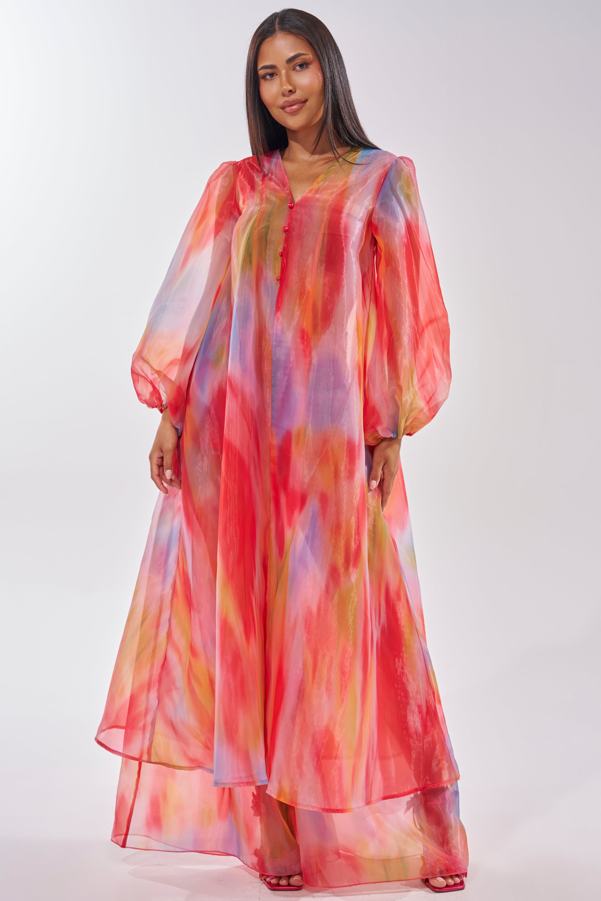 A woman models the INTERESTED IN YOU DUSTER, a long, sheer organza piece with billowy sleeves and a vibrant abstract pattern in red, yellow, pink, and blue, set against a plain light background. 3
