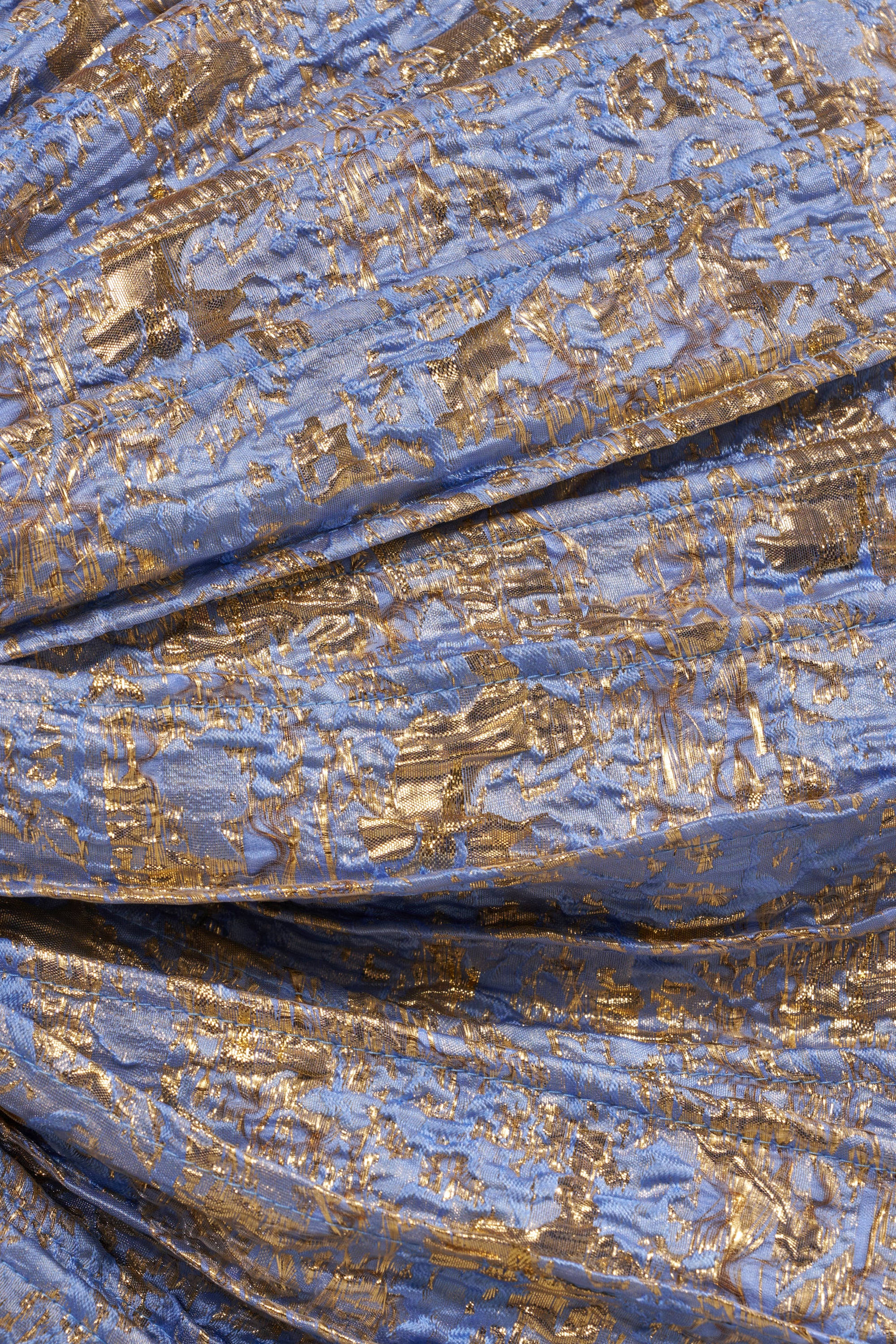 Close-up of GLORY BROCADE BLOUSE fabric—crumpled blue metallic brocade with an irregular gold pattern. Its textured, shimmering surface is ideal for a statement bow blouse or a dramatic top. 10