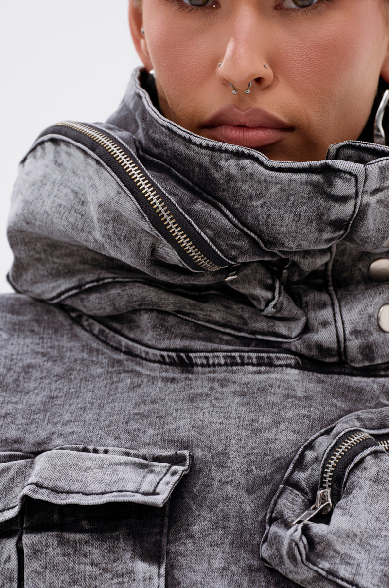 Close-up of a person wearing the MODEL BEHAVIOR DENIM TOP, an acid-wash black jacket with a high collar, silver zippers and buttons. A septum ring and just-visible lips complete their edgy look with a cropped vest style.