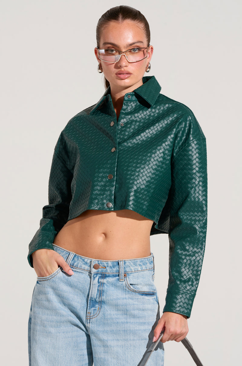 A person confidently stands in a LUXURY GIRL WOVEN PU CROPPED SHIRT IN GREEN paired with light blue jeans, their hair pulled back, complemented by transparent and stylish sunglasses.