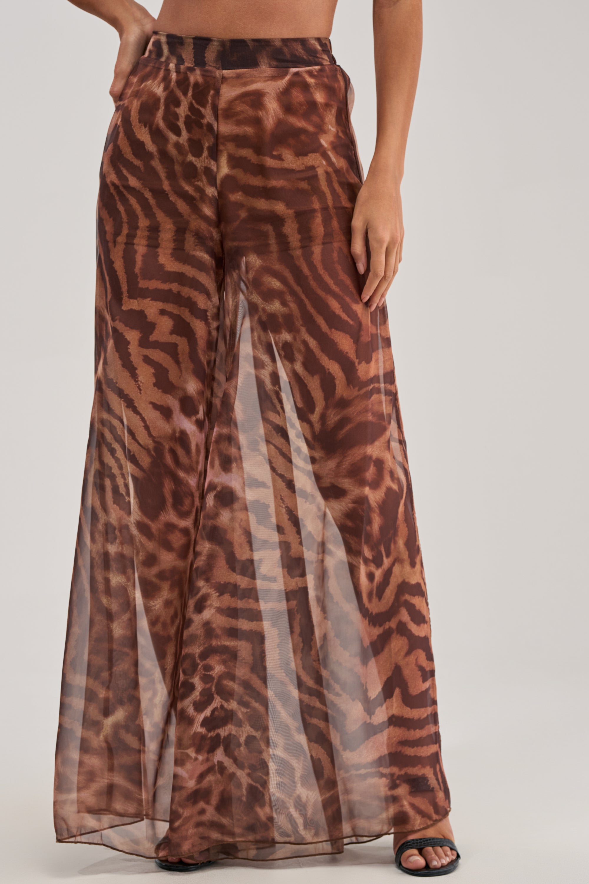A person styles the MOONLIGHT TIGER PALAZZO PANTS—high-waisted, wide-leg, and sheer—with open-toe black heels for a standout date night look.
