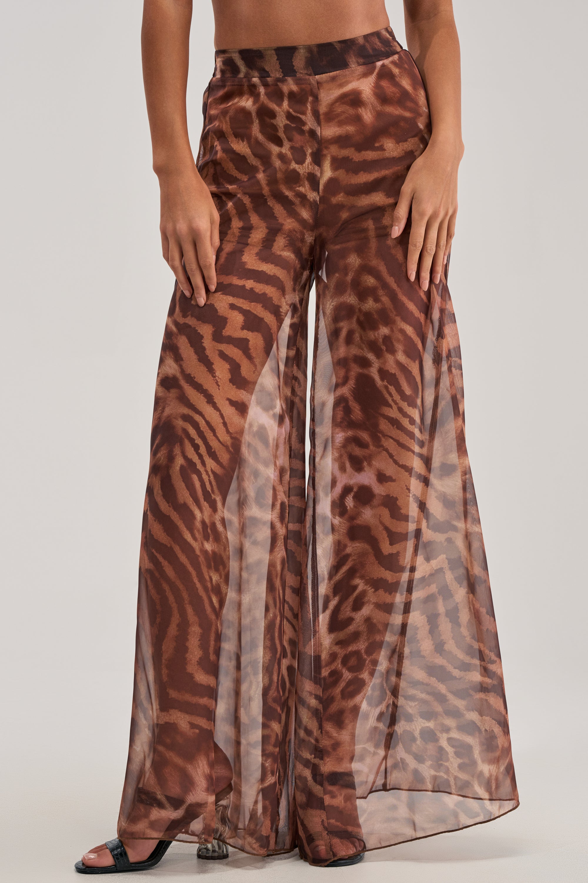 Wearing MOONLIGHT TIGER PALAZZO PANTS with a bold brown and black animal print, paired with open-toed black heels, creates a statement date night look that pops against a simple, neutral background.