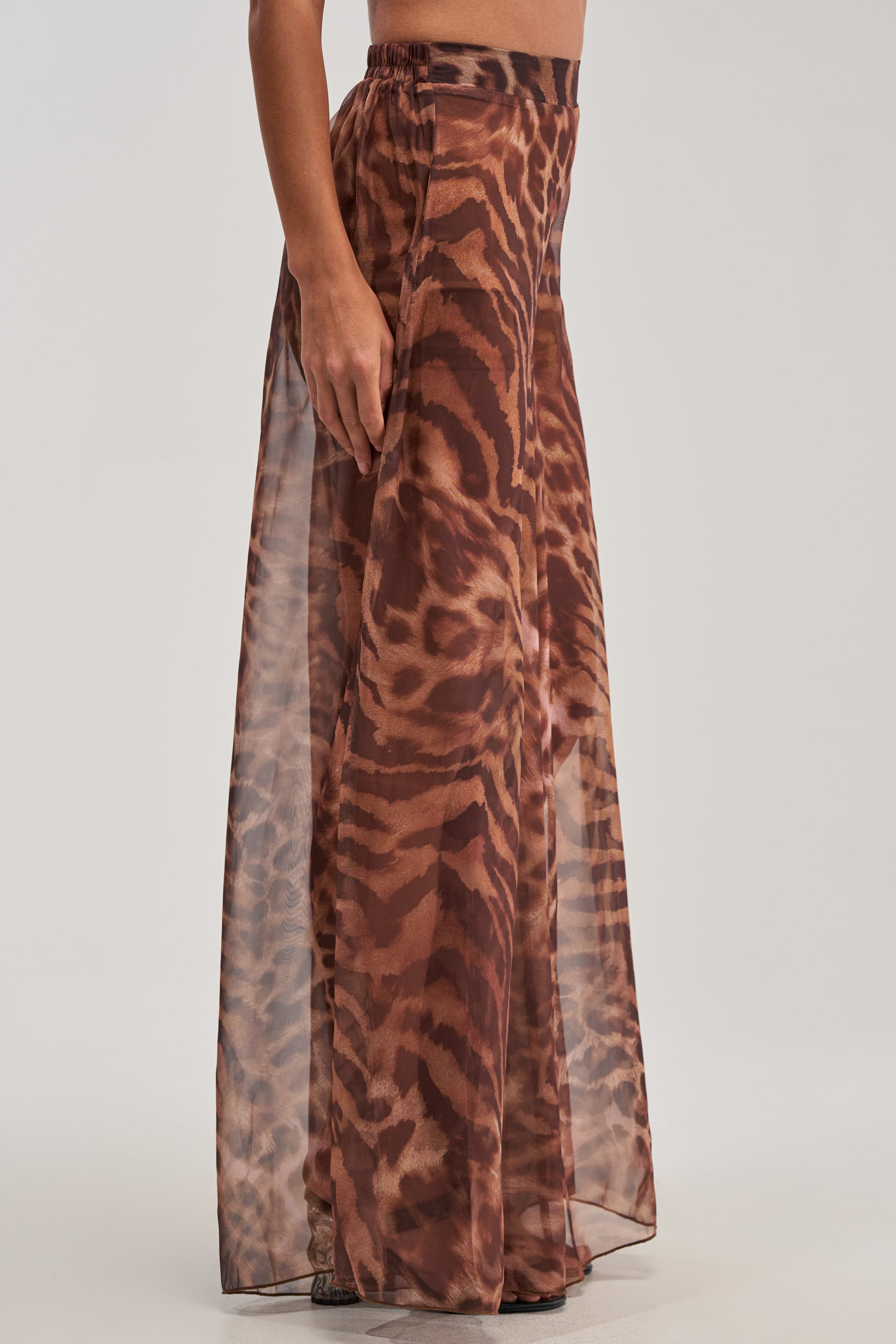 Wearing MOONLIGHT TIGER PALAZZO PANTS, a person stands against a plain light background, making a bold fashion statement with these sheer, floor-length tiger print pants.