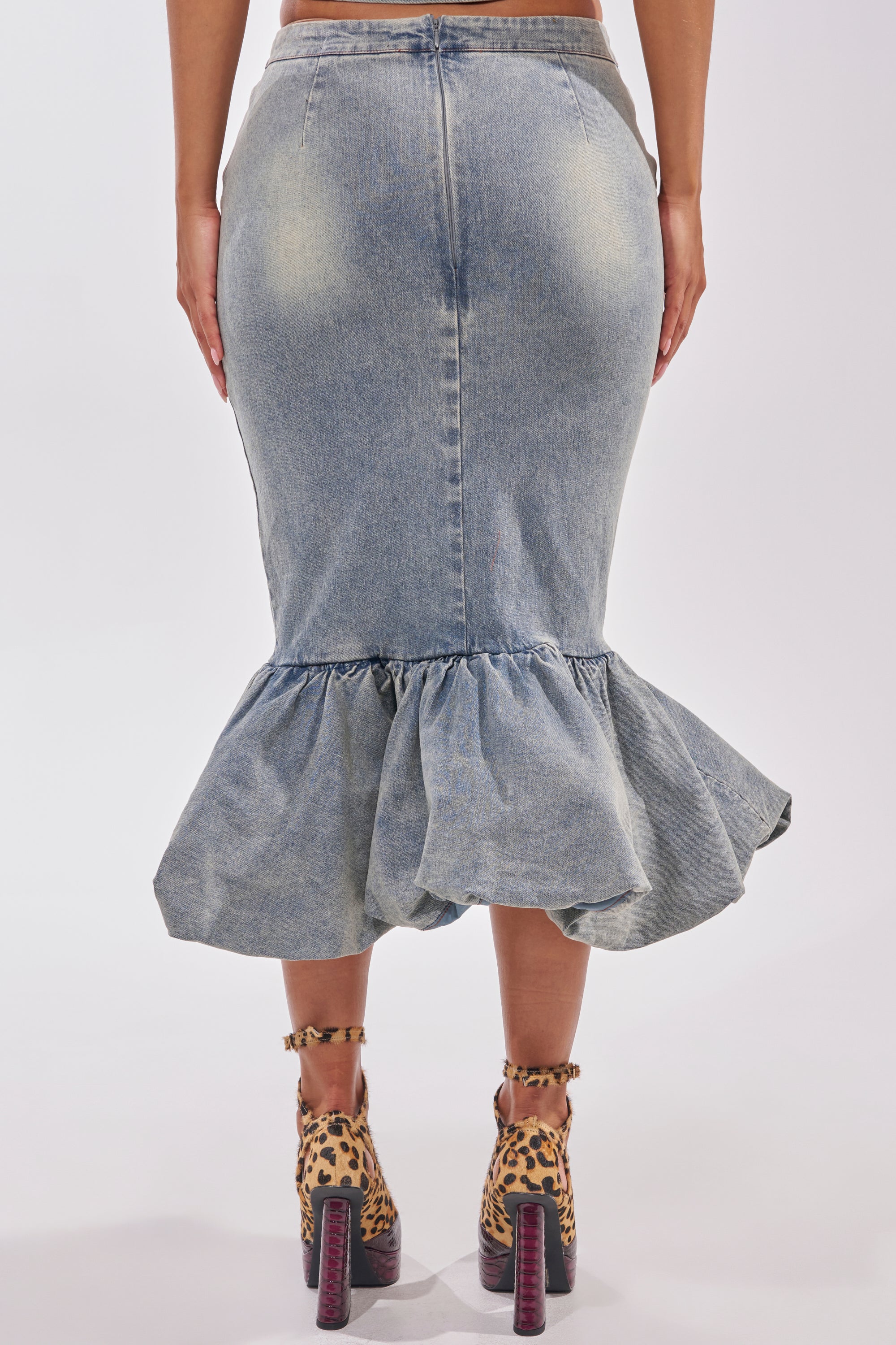 A woman models the JOSIE DENIM MIDI SKIRT with a ruffled hem, styled with tan leopard-print platform heels. She is shown from the back, standing against a plain background. 3
