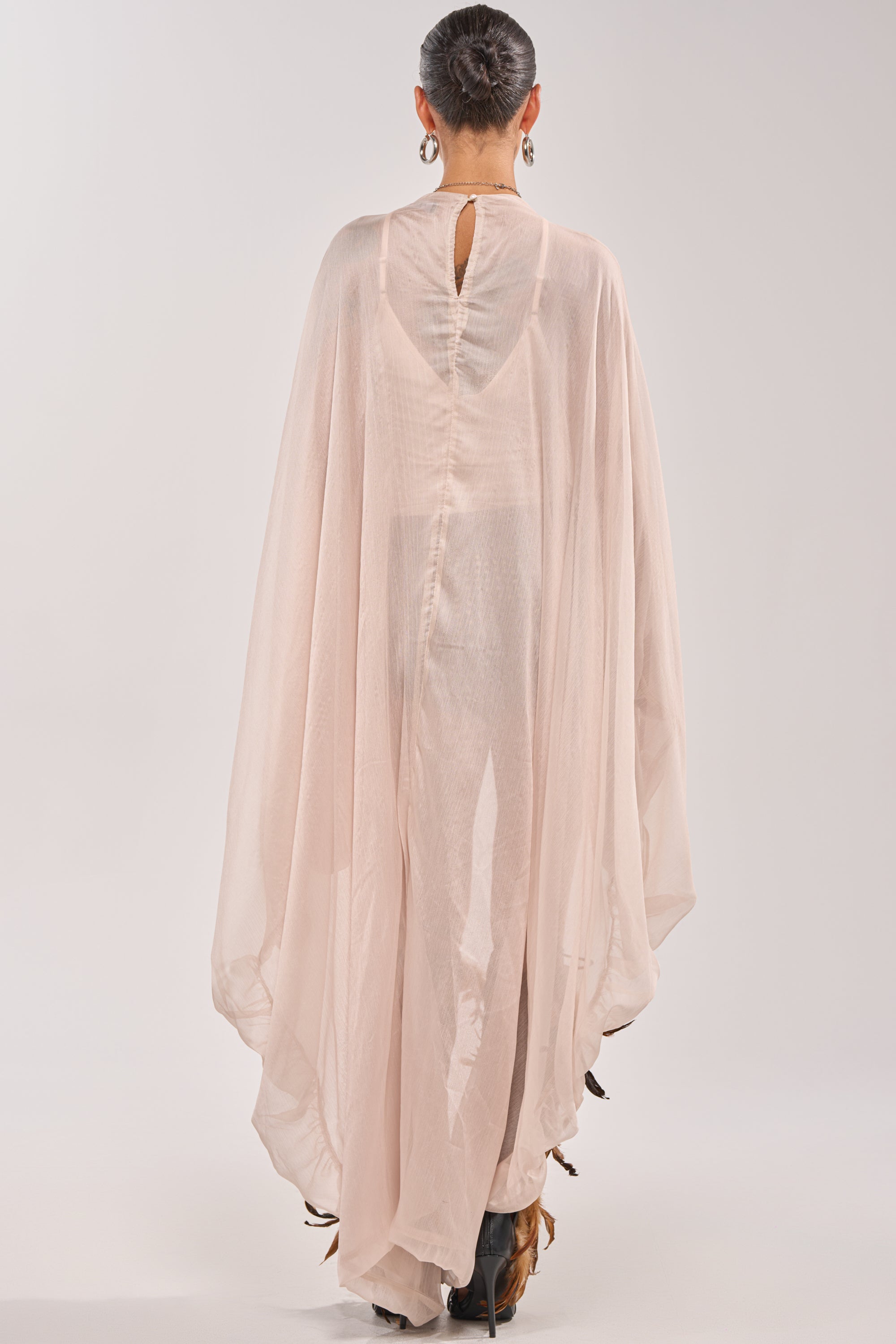 A person stands facing away, wearing the HEAD IN THE CLOUDS CHIFFON BLOUSE in light pink with sheer, flowing fabric and a keyhole back. Their hair is tied up and they wear hoop earrings. 5