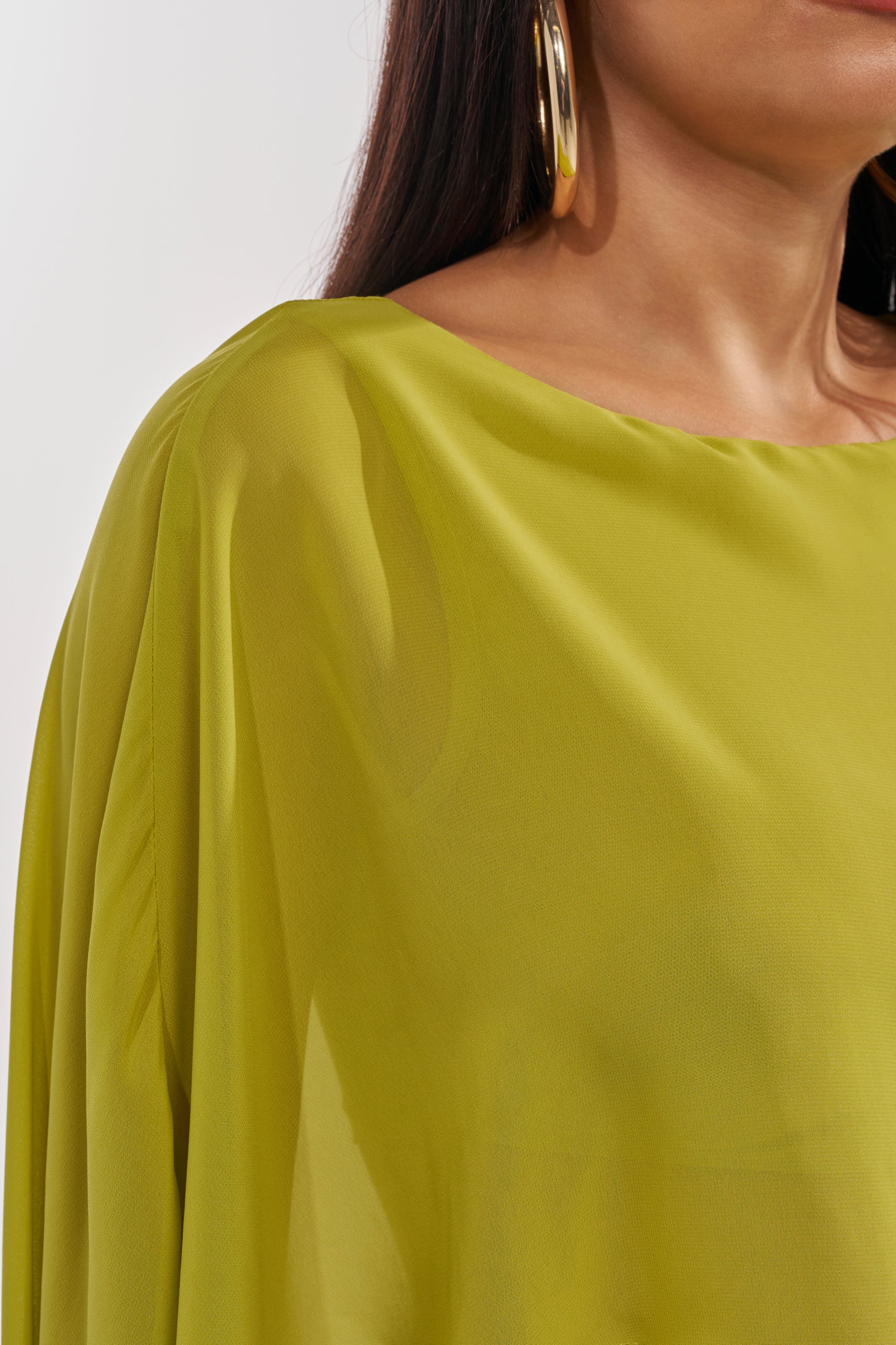 A close-up of a woman in the IT GIRL BLOUSE IN CHARTREUSE—a sheer chiffon top—paired with large gold hoop earrings, showcasing effortless resort wear style with her shoulder, neck, and part of her face visible. 7