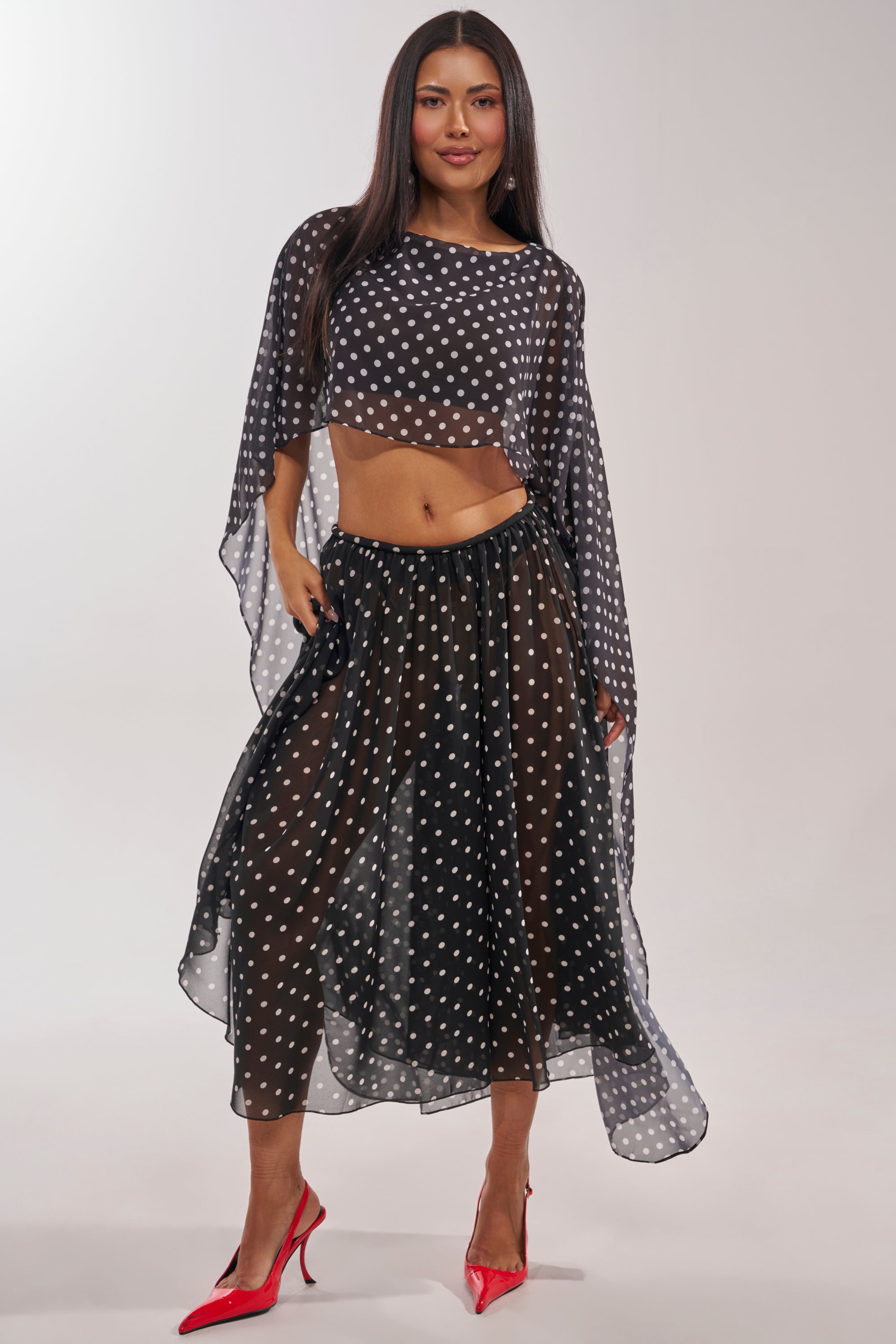 A woman in the IT GIRL BLOUSE paired with a matching flowy skirt, red heels, and long straight hair smiles against a plain background, showcasing chic statement layering. 2
