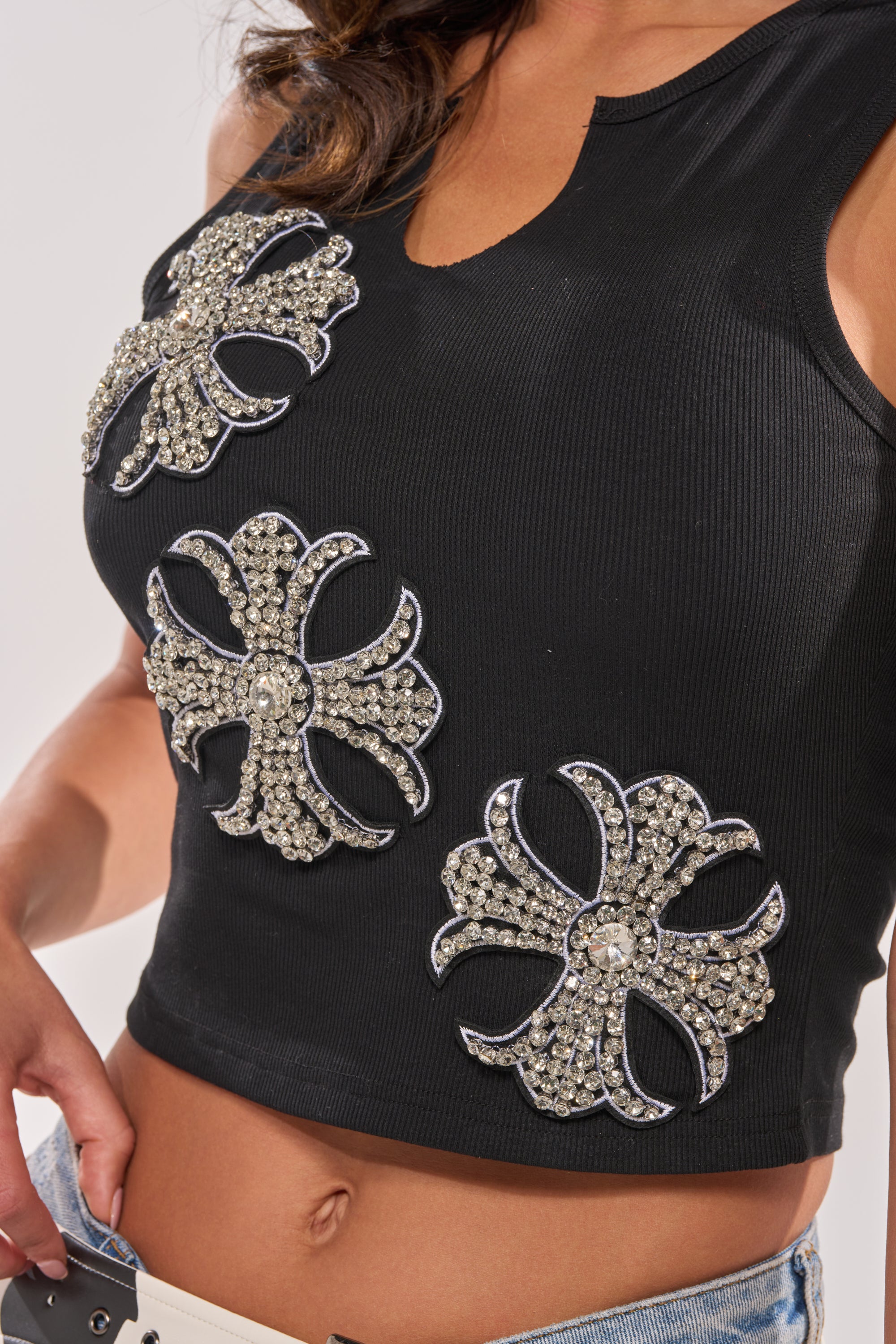 A person wearing the COLD HEARTED RHINESTONE TANK—a sleeveless top featuring three large, ornate silver rhinestone flower designs. Only the torso and part of one arm are visible. 8