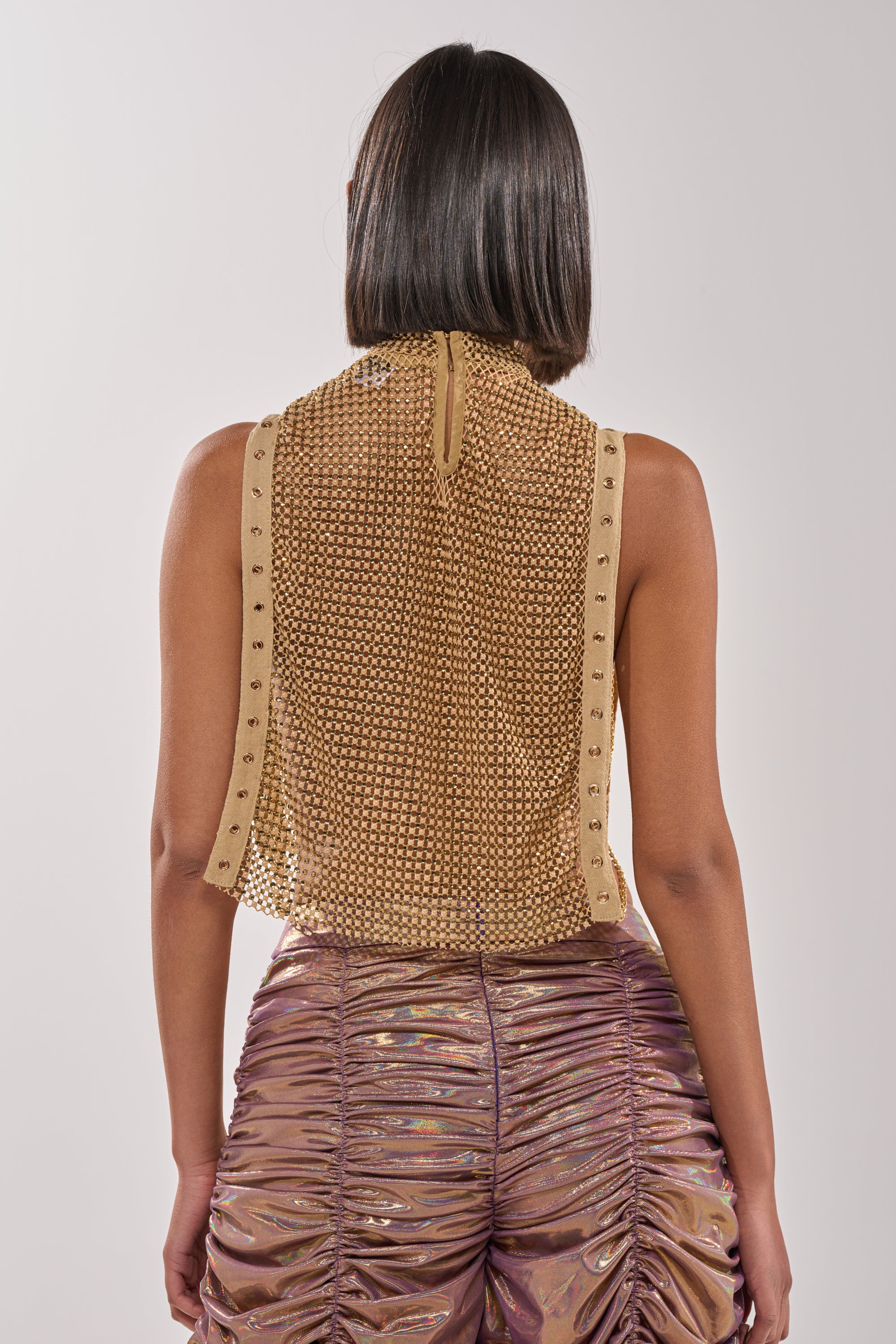 A person with straight shoulder-length hair is shown from the back, wearing the TEARS IN THE CLUB OPEN SIDES MOCK NECK RHINESTONE MESH BLOUSE and shiny, ruched metallic purple pants against a plain light gray background. 5