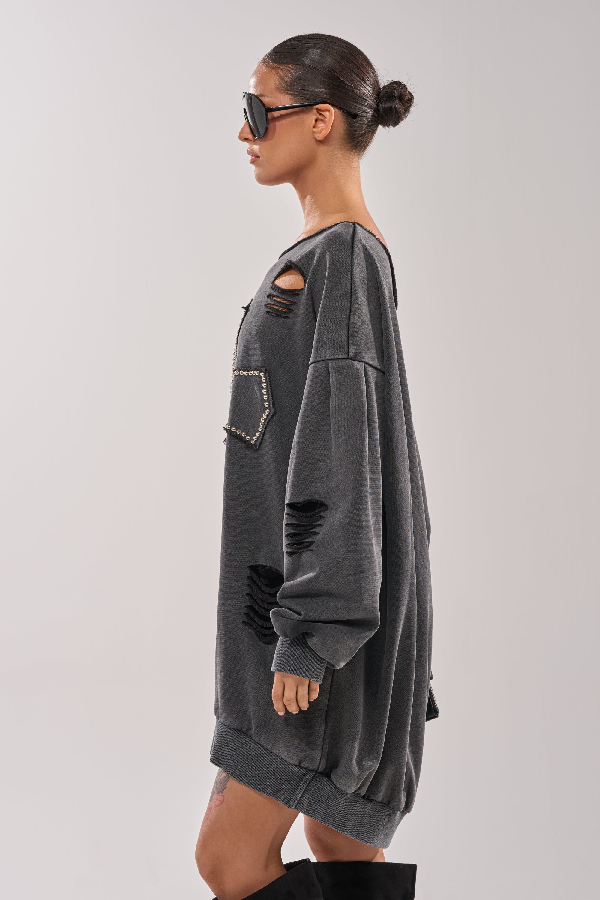 Wearing the LEX STUDDED MINI SWEATSHIRT DRESS, a woman with slicked-back hair and large sunglasses stands in profile against a light background, paired with black knee-high boots. 3