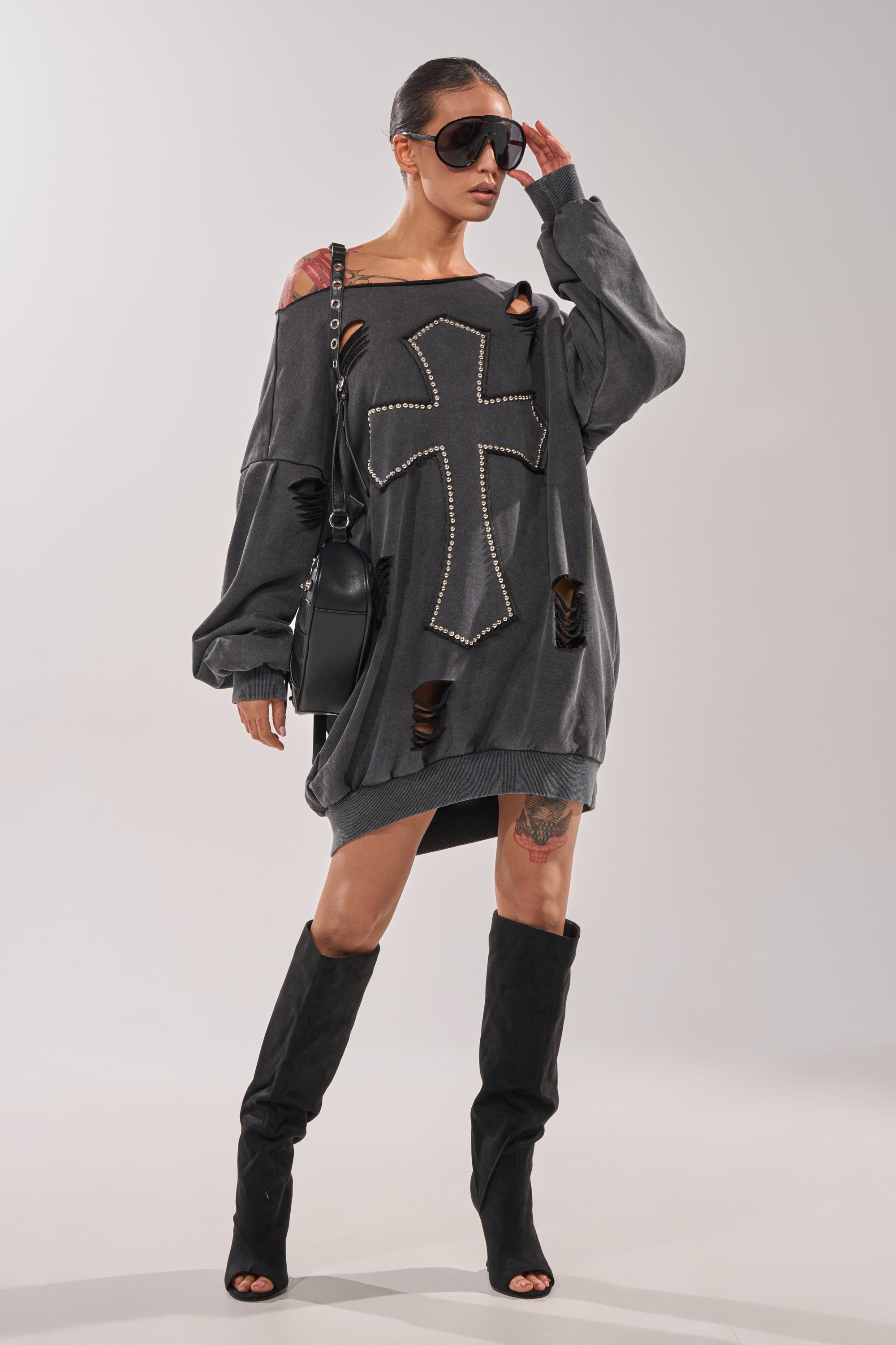 A woman in sunglasses confidently poses against a plain background wearing the LEX STUDDED MINI SWEATSHIRT DRESS styled with a black mini dress, black handbag, and knee-high boots. 6