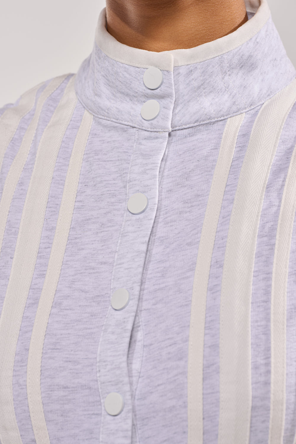 Close-up of the BIG SPORTS GIRL JUMPSUIT in light grey cotton, featuring a high collar, vertical cream stripes, round white front buttons, and a softly textured fabric. 6
