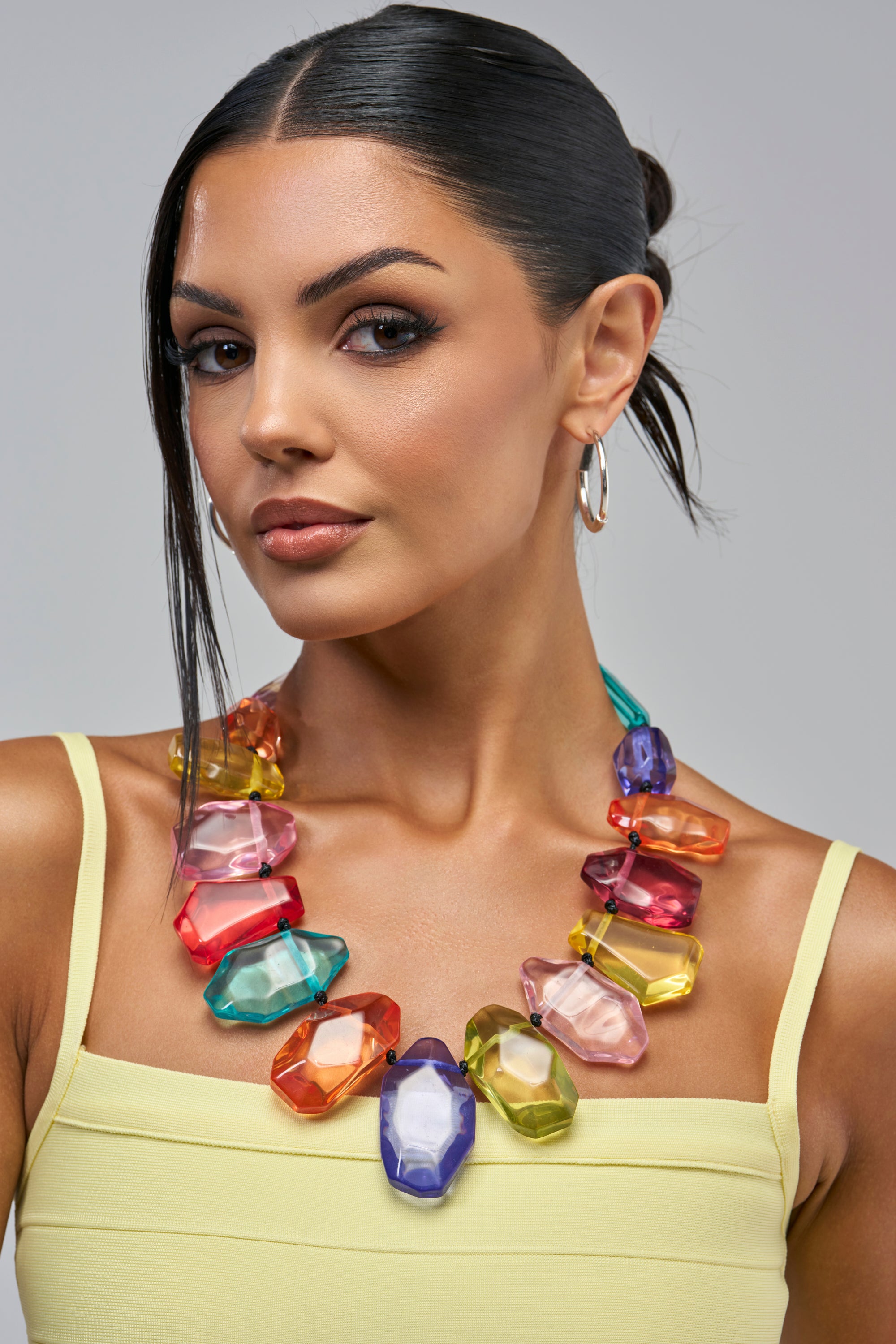 A person wearing the COLOR ME PRETTY GEMSTONE NECKLACE IN MULTI, a chunky necklace featuring large, multi-colored translucent geometric beads.