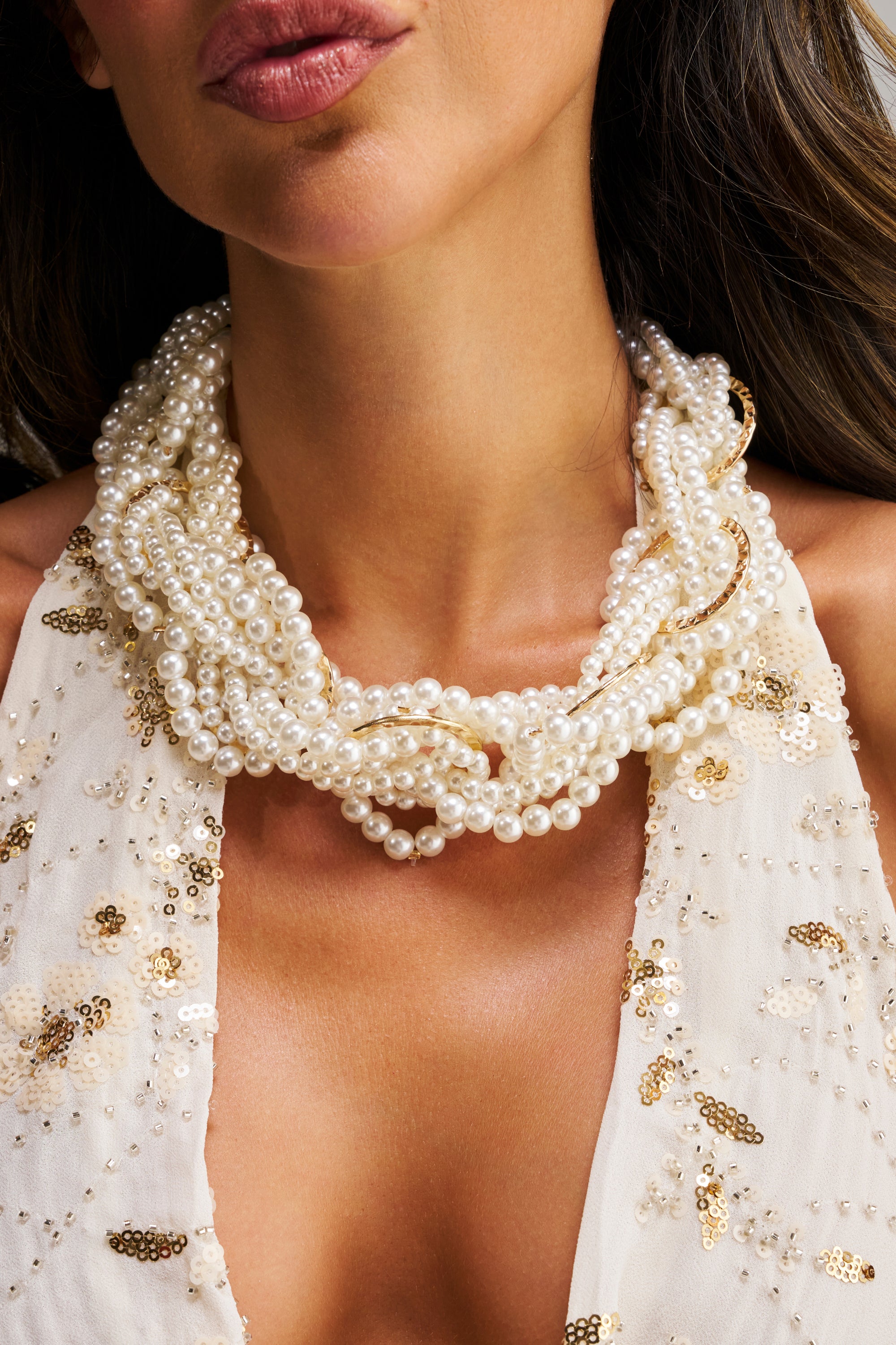 A woman wearing the SHARON NECKLACE, a formal multi-strand pearl piece, paired with a cream sequined deep-neckline dress; only her lower face and neck are shown.