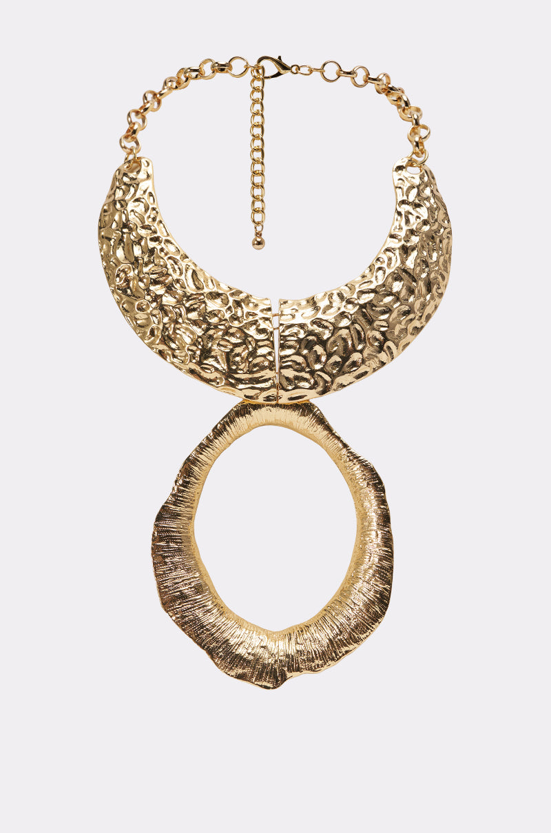 The MOLTEN NECKLACE is a gold statement piece with a sculpted collar, ornate textured details, and a large, irregular oval pendant, displayed against a plain light background.