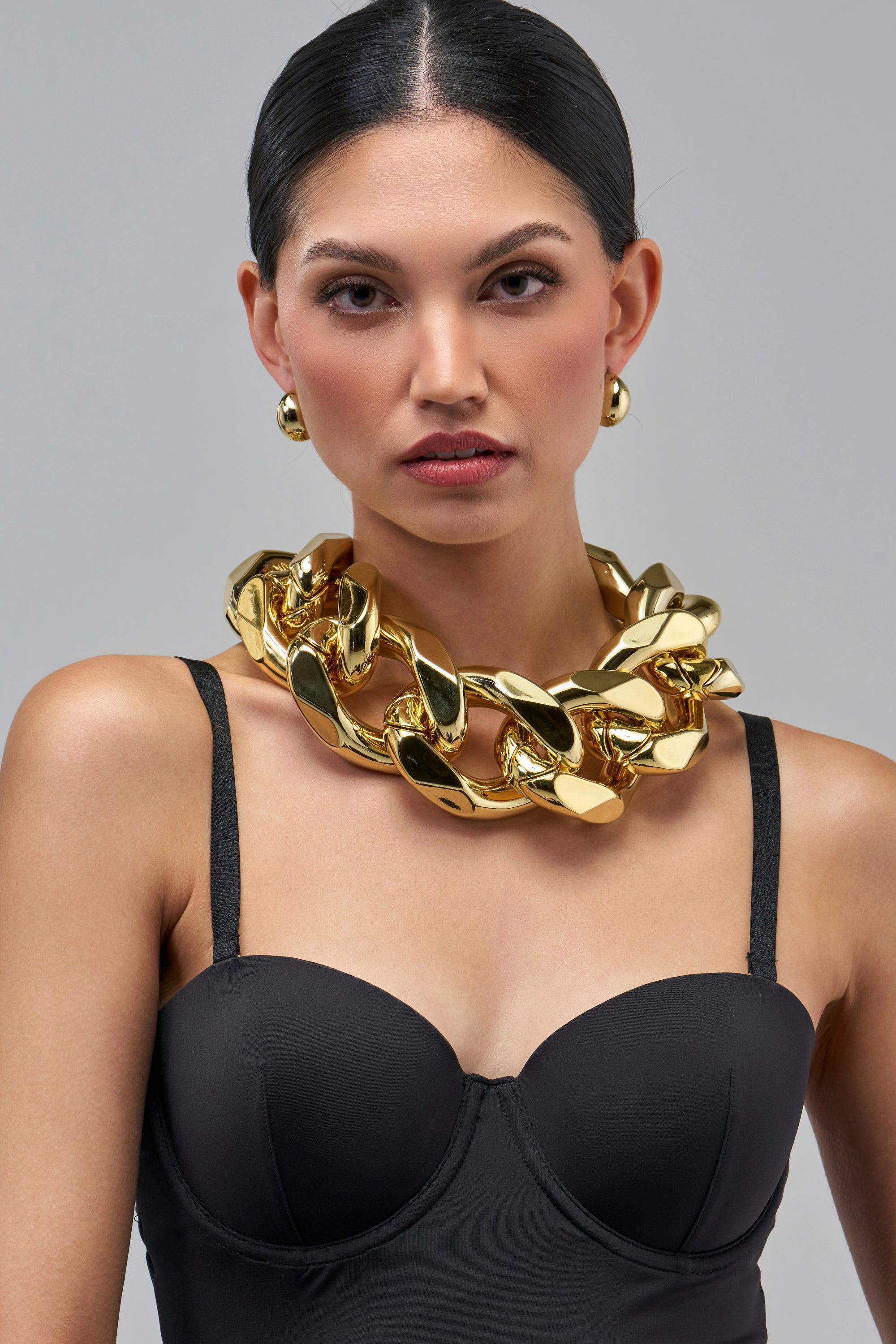 A person wearing an ICON BEHAVIOR LINK NECKLACE with edgy, chunky, oversized gold-tone links and matching stud earrings.
