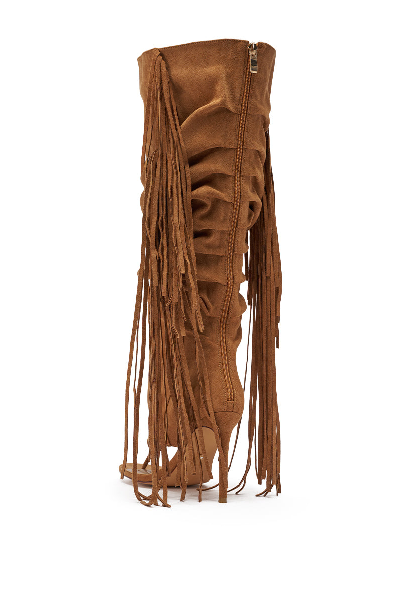 The AZALEA WANG JOHANNA Tan Fringe Gladiator Sandal features faux suede, knee-high stiletto heels, ruched details, and long fringe accents along the sides, displayed from a side view on a white background. 4