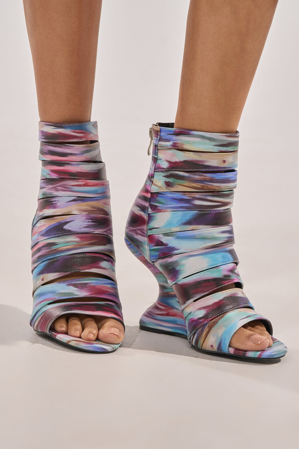 A close-up of feet in the AZALEA WANG JOHANNES MULTI RAINBOW WEDGE OPEN TOE BOOTIE, featuring colorful abstract patterns and a unique inverted wedge heel, set against a neutral background. 2