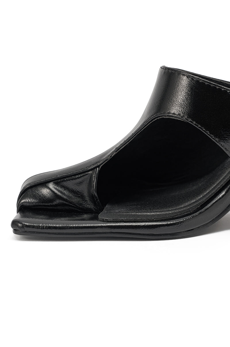 Close-up of the AZALEA WANG JONENE BLACK STILETTO MULE, featuring black faux leather, a split square toe, curved partial upper, and a sleek stiletto heel, set against a white background. 6