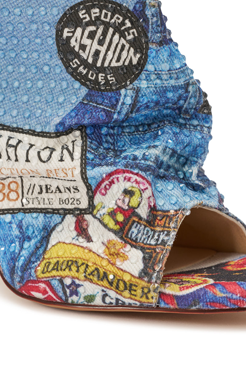 Close-up of the AZALEA WANG JONICE BLUE MULTI RHINESTONE OPEN TOE BOOTIE, a blue textured shoe with colorful patches, cartoon graphics, and labels like "Sports Fashion Shoes" and "Dairy Leader." Features an open toe design. 5