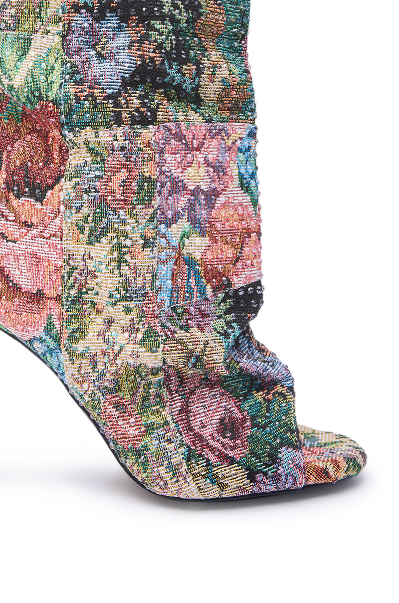The AZALEA WANG JONICE Floral Rhinestone Embellished Open Toe Bootie features a close-up of colorful floral tapestry and sparkling rhinestones on a chic stiletto heel, showcasing shades of pink, green, yellow, and blue.