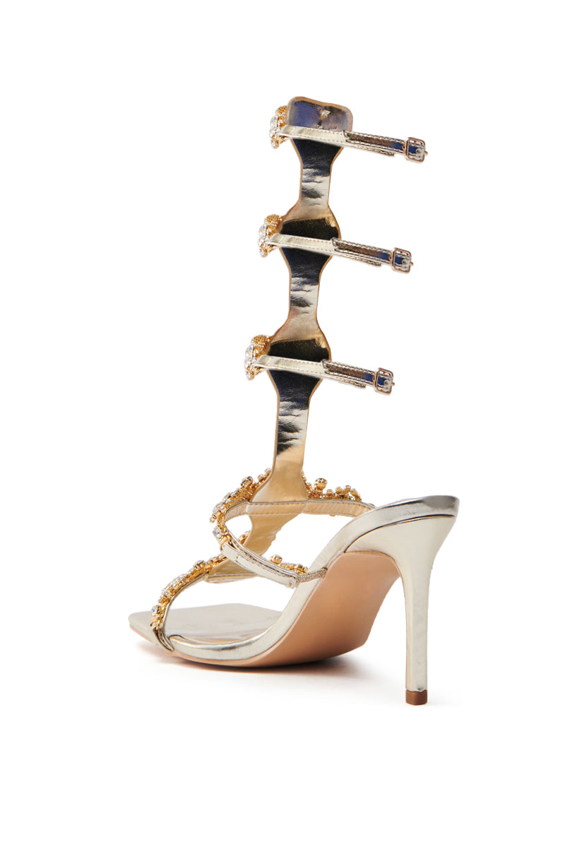 The AZALEA WANG JONQUIL GOLD EMBELLISHED GLADIATOR SANDAL features metallic faux leather, rhinestone-adorned straps, and an elegant back with decorative extensions.