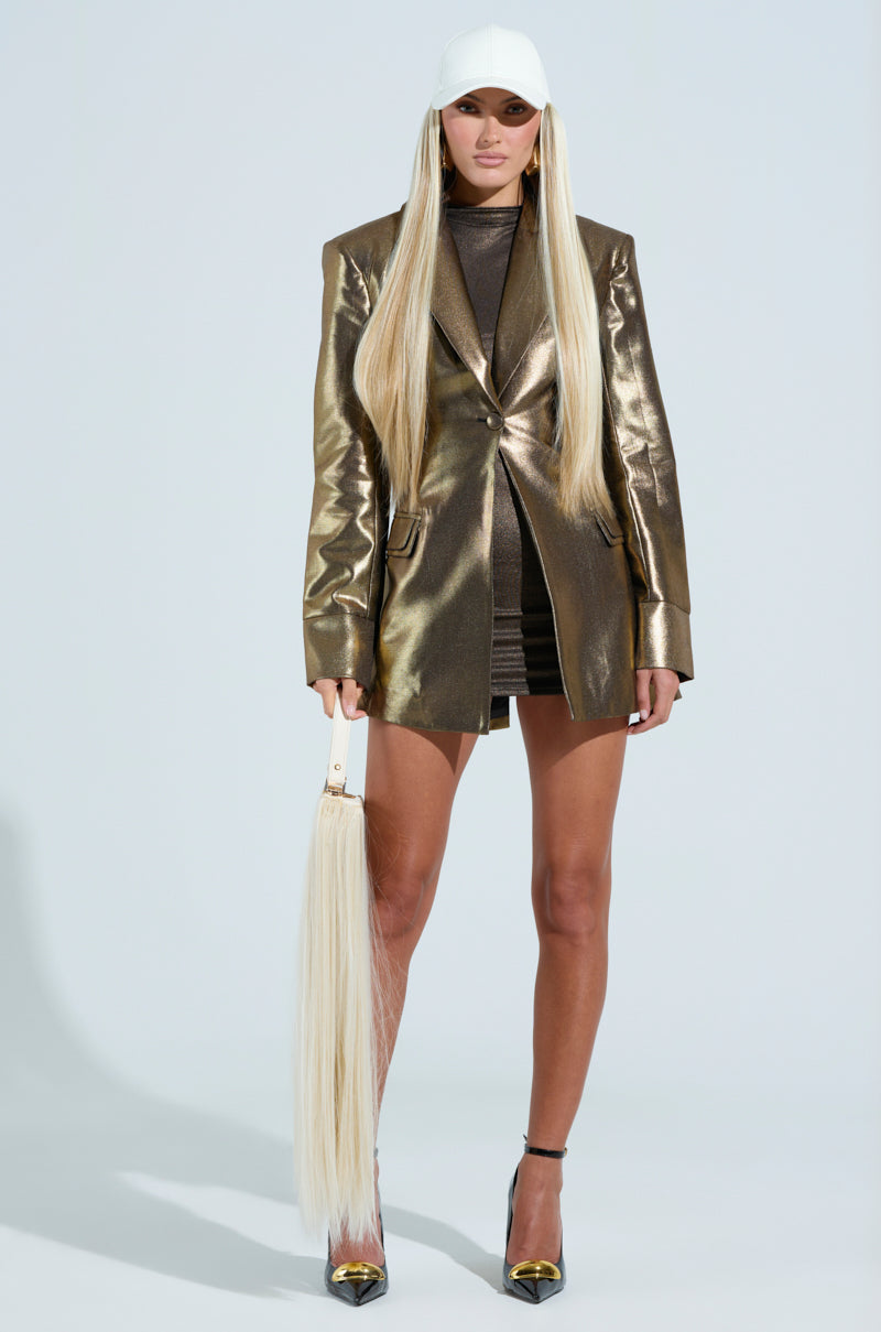 Wearing the JOSH'S GOLD MEDAL JACKET, a black turtleneck mini dress, and black heels, they exude confidence. Their long straight blonde hair pairs with a handbag styled like a ponytail, while a white cap adds effortless flair to the look.