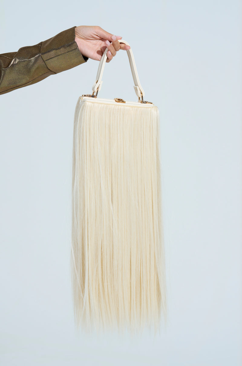 A hand holds the JOSHIE SYNTHETIC HAIR TRUNK PURSE, a striking handbag featuring long, straight, hair-like material and a structured handle set against a light background.