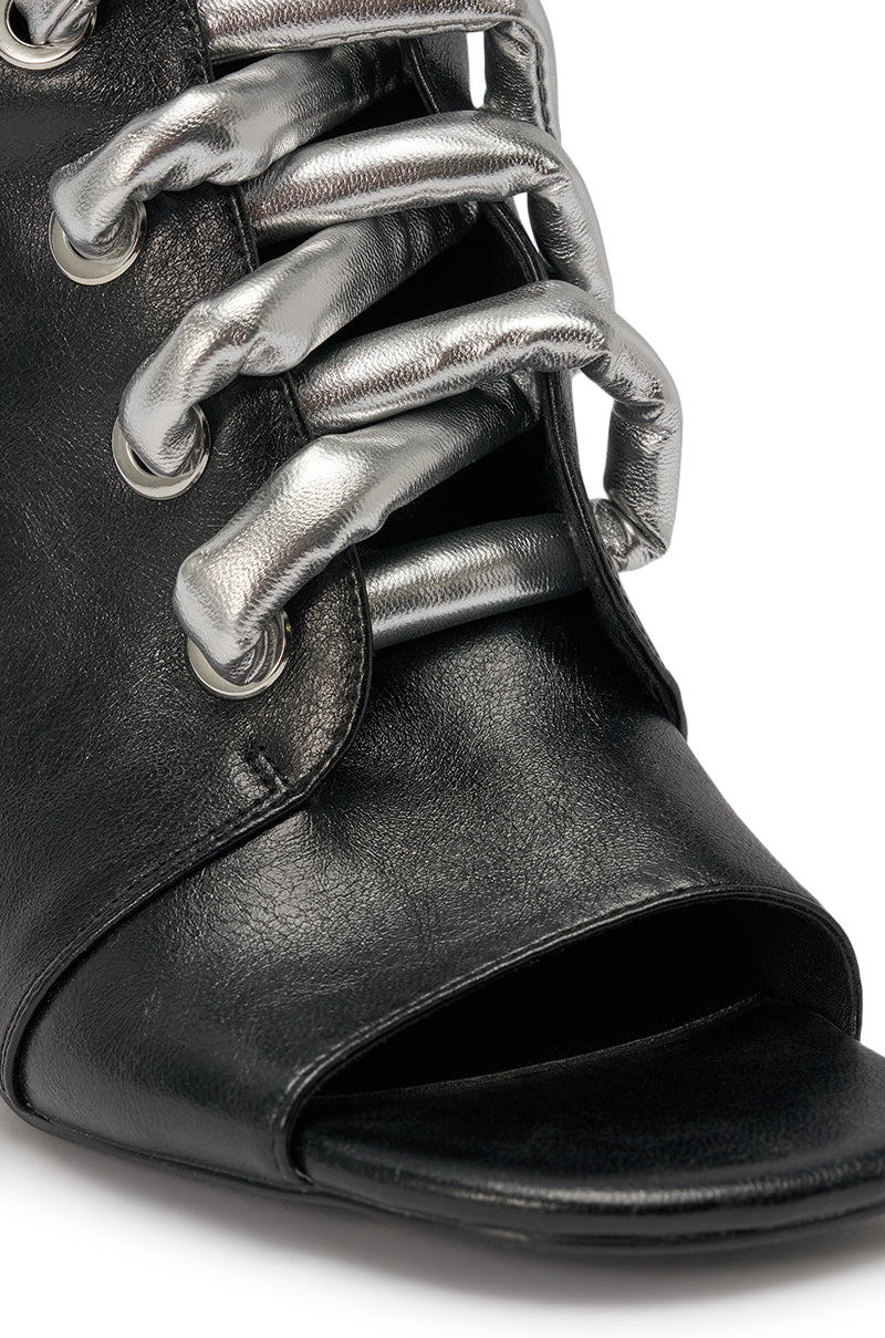 Close-up of the AZALEA WANG JOSS BLACK BLOCK LACE OPEN TOE BOOTIE, featuring black faux leather, metallic silver padded laces through large eyelets, and a stylish block heel. 6