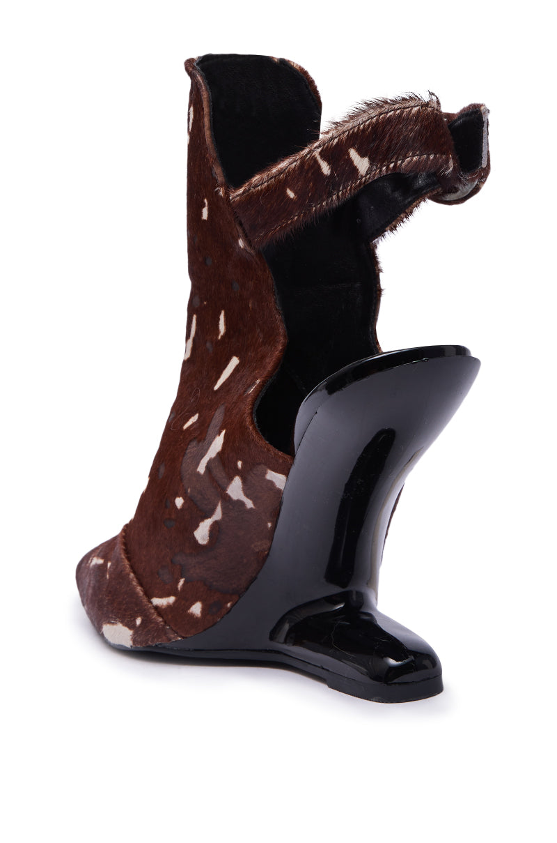 The AZALEA WANG JOST BROWN MULTI WEDGE PUMP features a cow print in brown and white genuine calf hair, a high wedge heel, and a sculpted black heel, shown from the back and slightly to the side.