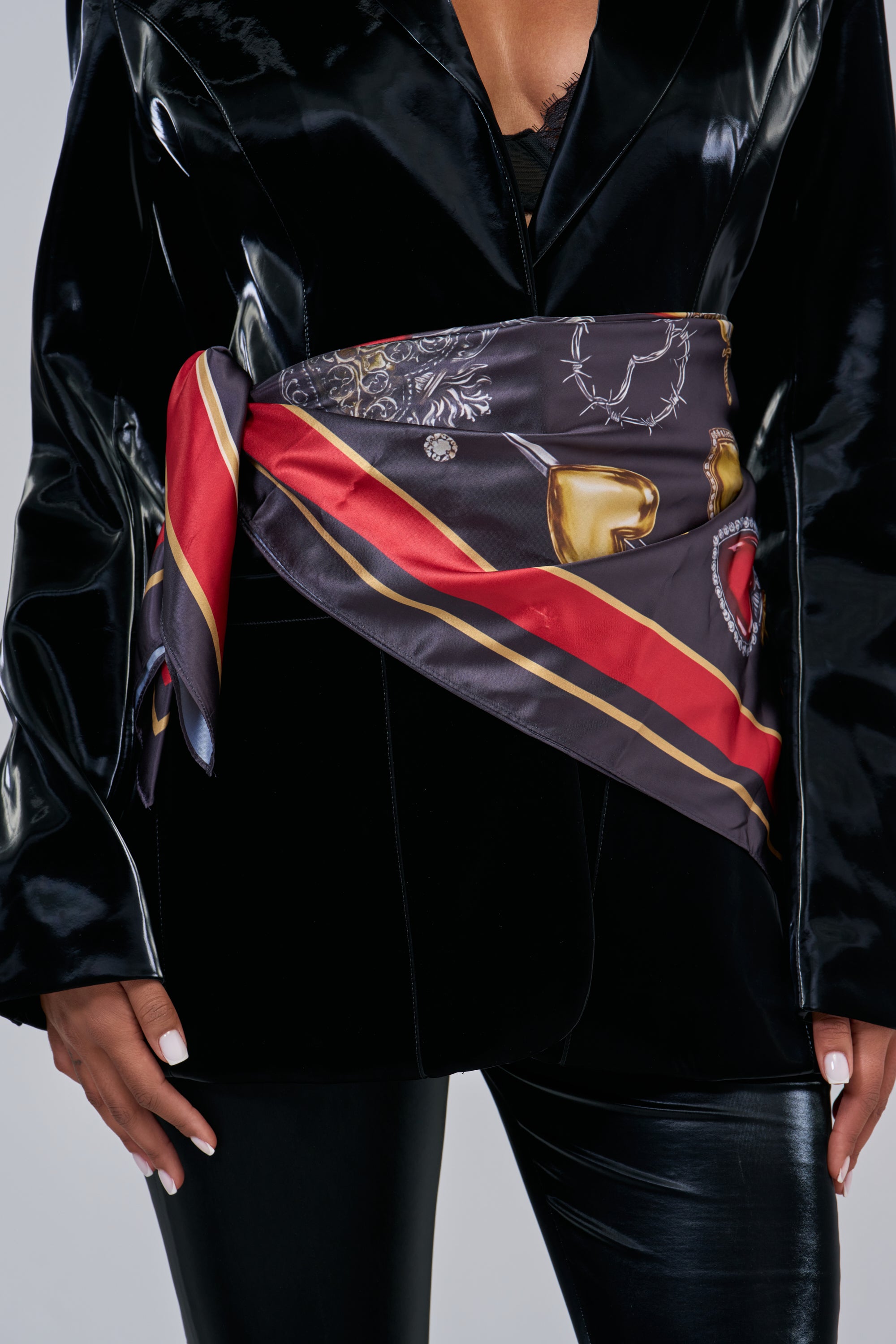 A PIERCED HEART SATIN SCARF featuring golden hearts and barbed wire, tied as a belt over a black jacket for an edgy streetwear look.