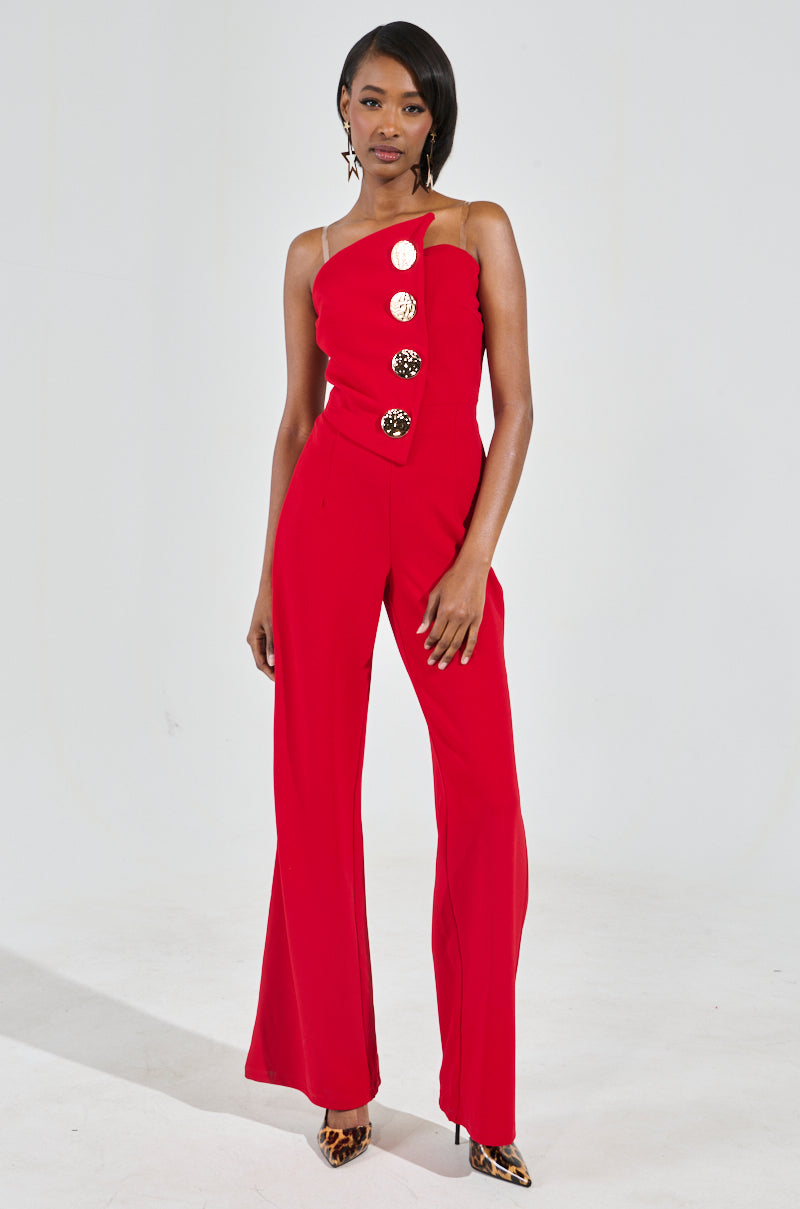 A woman stands confidently in a chic piece: the Baddie Strapless Jumpsuit, featuring an eye-catching bright red color and embellished with gold buttons along the front. She pairs it with leopard-print shoes and star-shaped earrings, her hair styled straight, against a plain light-colored background.