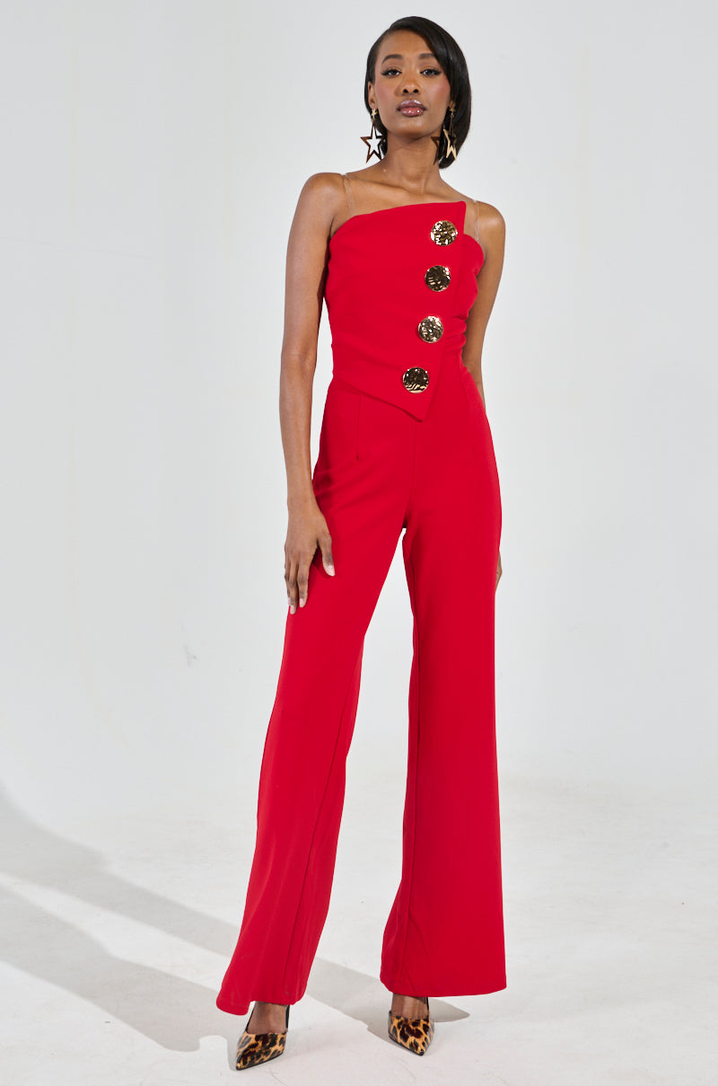 Against a light gray background, a woman confidently models the BADDIE STRAPLESS JUMPSUIT WITH GOLD BUTTONS in red. She accentuates her chic look with hoop earrings and leopard print heels, exuding style and flair effortlessly.