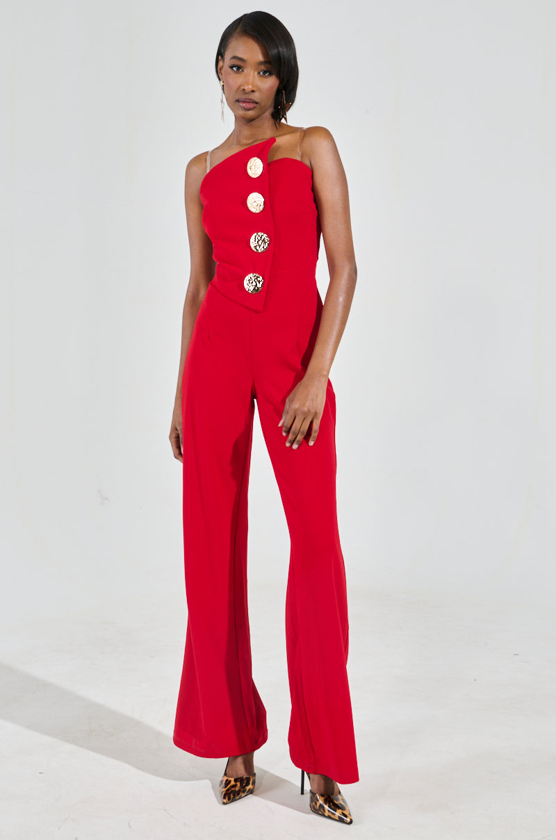 A person flaunts a chic piece—a vibrant red BADDIE STRAPLESS JUMPSUIT WITH GOLD BUTTONS. Paired with leopard print heels, they stand confidently against a plain light background, exuding a poised elegance.