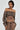 A woman wears the BROKE MY HEART OFF THE SHOULDER SWEATSHIRT, exhibiting a fashionable lace-up back closure in a brown hue, complemented by matching high-waisted pants. She enhances her look with hoop earrings and straightened hair, while the plain background accentuates her chic outfit.