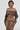 Wearing the 'BROKE MY HEART OFF THE SHOULDER SWEATSHIRT,' a person dons a brown off-the-shoulder top with long sleeves, paired with a matching skirt featuring a lace-up back closure. Against a plain background, they accessorize with hoop earrings and have styled hair, gazing slightly to the side.