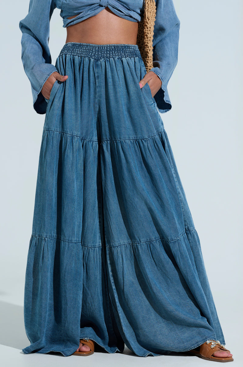 A person wears the PERFECT AS CAN BE PANT, showcasing ultra-wide-leg tiered denim with a comfy high-rise seersucker waistband, and casually stands with hands in the pants' pockets.