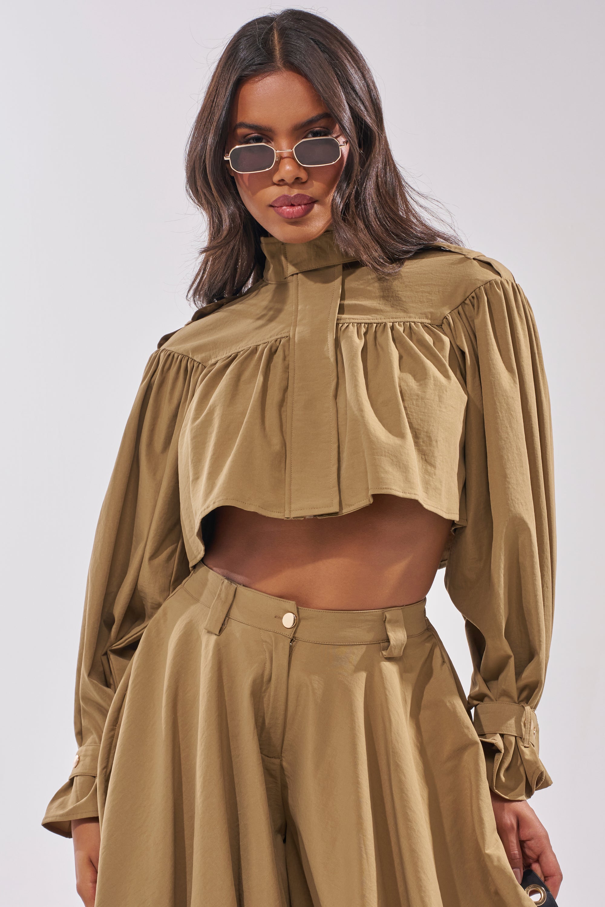 Woman wearing the CANT STOP WONT STOP BUTTON DOWN—a stylish, high-neck, long-sleeve cropped top with voluminous sleeves and matching high-waisted, wide-leg pants—standing against a light background with sunglasses. 1
