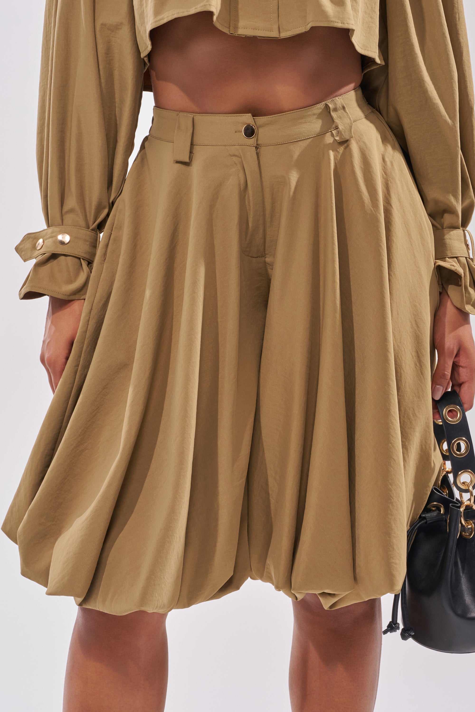 A person wears the CANT STOP WONT STOP BERMUDA SHORT, paired with a matching cropped long-sleeve top. They hold a small black handbag in their right hand. 1