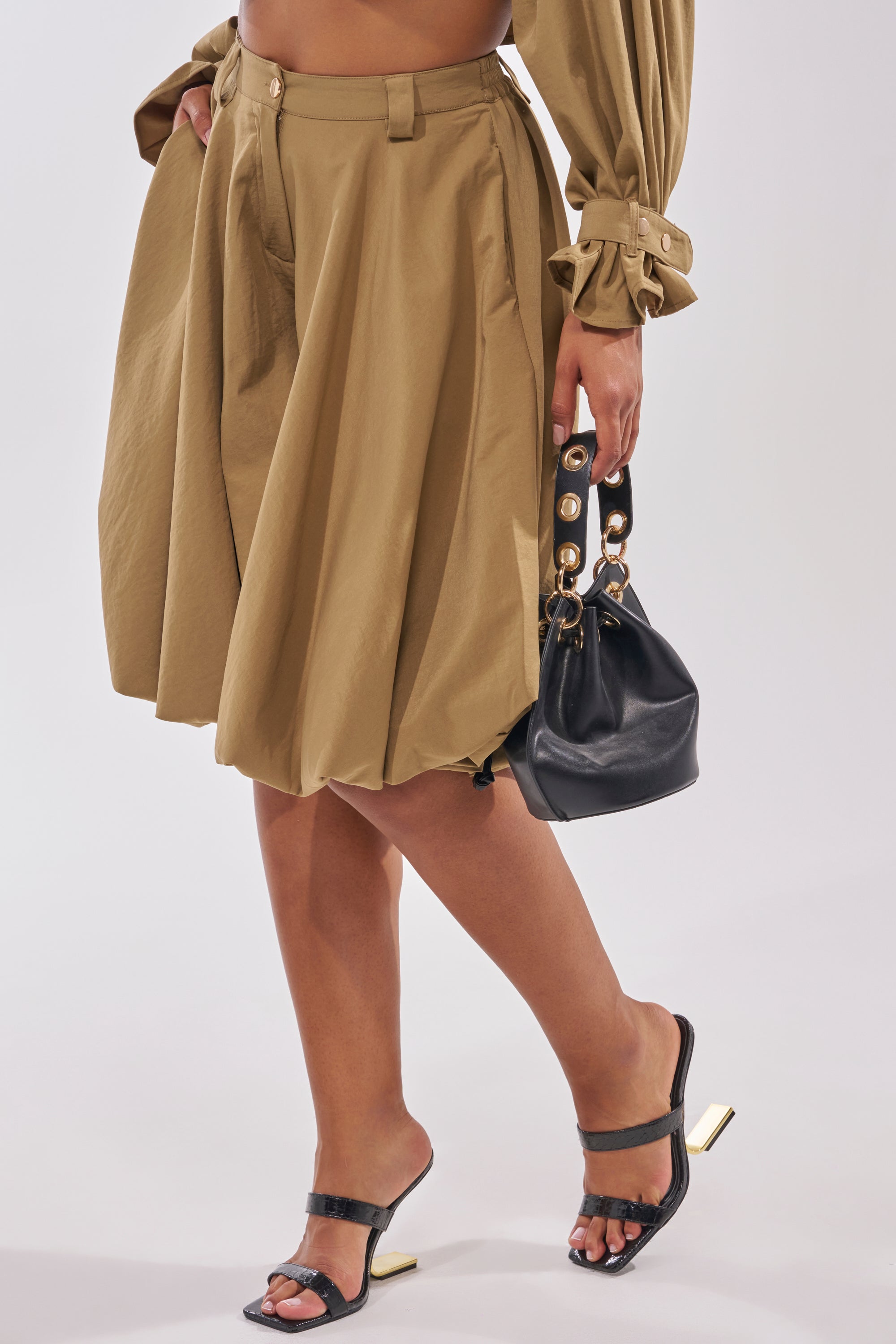 A person wearing the CANT STOP WONT STOP BERMUDA SHORT, a matching long-sleeve top, black heeled sandals, and holding a small black handbag with gold accents stands against a plain background. 3