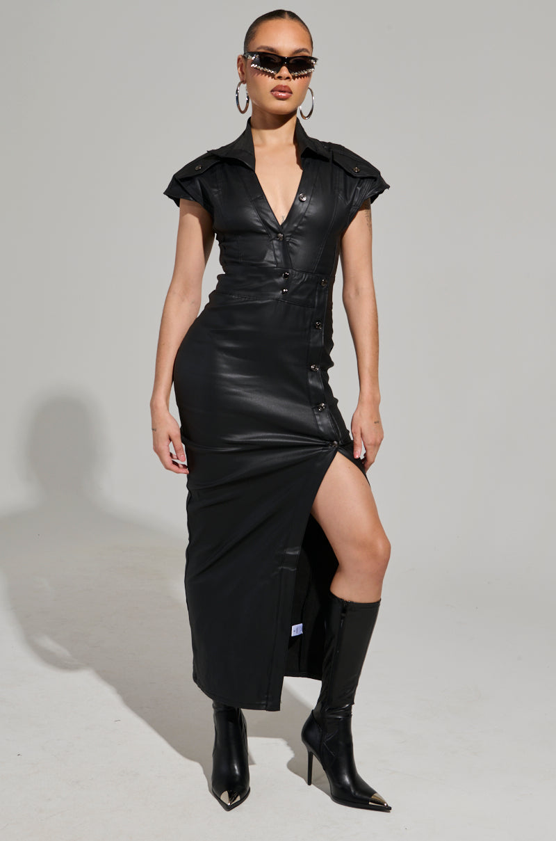 Dressed confidently in the CHELSEA BUTTON SIDE PU MAXI DRESS featuring a daring thigh-high slit, they showcase their style with pointy high-heeled boots, oversized hoop earrings, and chic sunglasses. Their hair is sleekly pulled back, enhancing the bold and modern aesthetic.