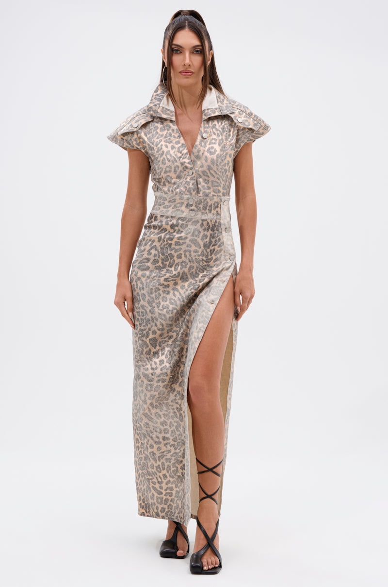 Wearing the TOO BUSY TO CARE LEOPARD MIDI DRESS, a woman stands against a white background. The curve-hugging dress features a bold leopard print, high slit, dramatic collar, and short sleeves, styled with black strappy sandals.