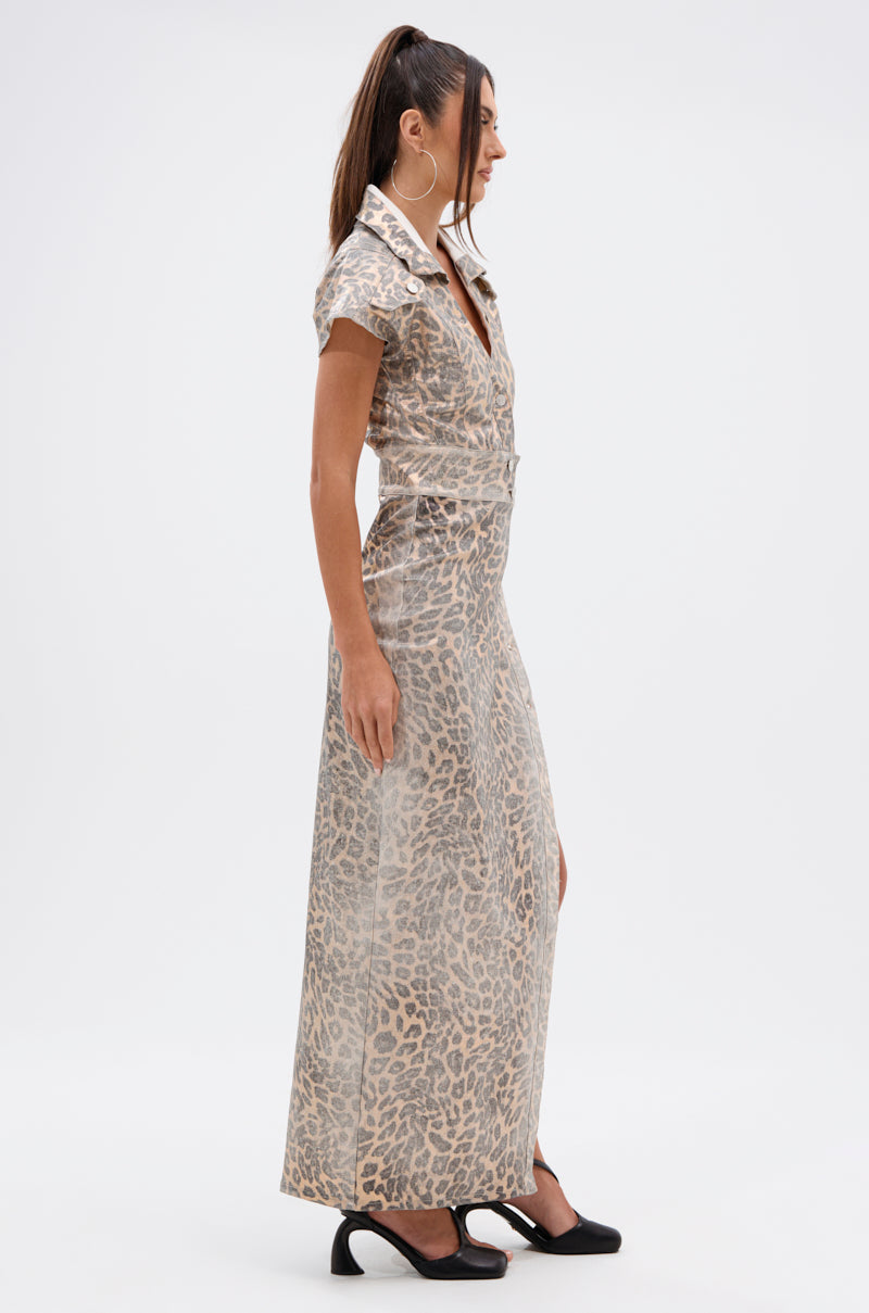 A woman stands in profile against a plain white background, wearing the TOO BUSY TO CARE LEOPARD MIDI DRESS—a curve-hugging, short-sleeved, collared leopard print midi dress with buttons—paired with black heels and a high ponytail.