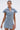 A woman models the NEVER TOO MUCH DENIM MINI DRESS—a short-sleeve, collared mini with a side slit—styled with layered necklaces and hoops against a light backdrop, making it your perfect day-to-night look.