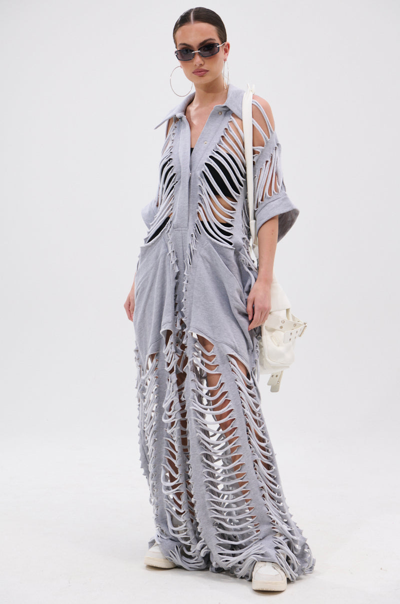 A person wears the OVER IT DISTRESSED FRENCH TERRY JUMPSUIT in heather grey with bold cutouts, paired with sunglasses, large hoop earrings, white sneakers, and a white bag, standing against a plain white background.