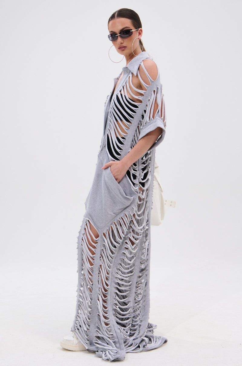 Wearing sunglasses and hoop earrings, a woman poses against a white background in the OVER IT DISTRESSED FRENCH TERRY JUMPSUIT, layered over a black outfit with white sneakers and a matching white bag.